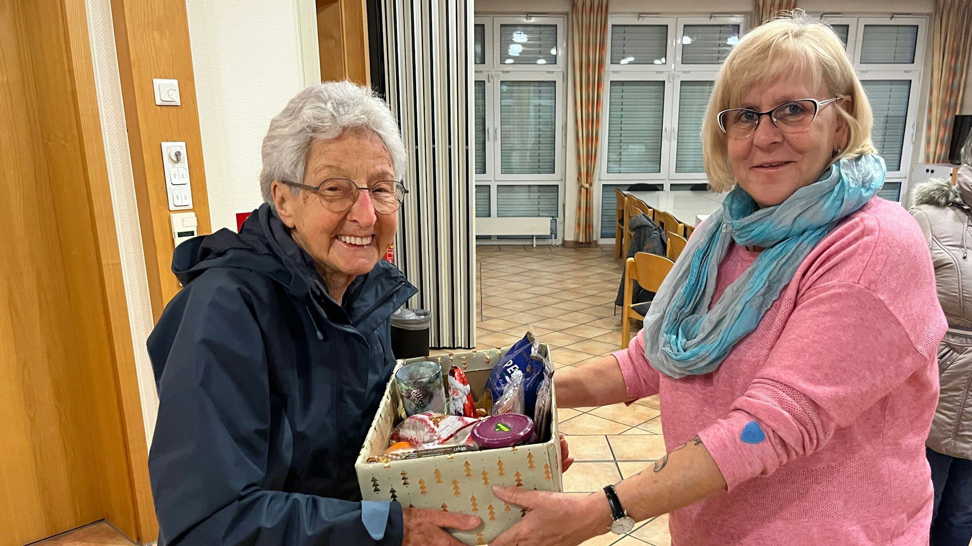 Eine ältere Frau überreicht einer anderen ein Paket mit Lebensmittel.