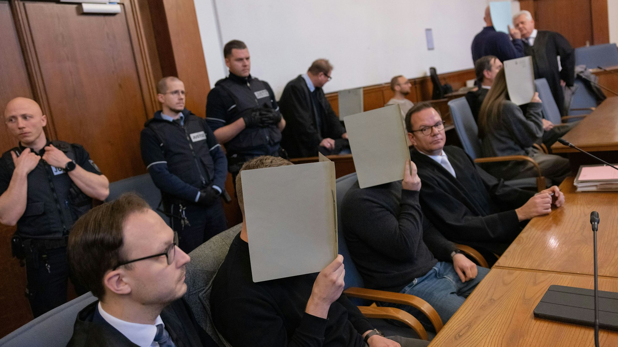 Die fünf Angeklagten Polizeibeamten im Gerichtssaal des Landgerichts. Sie halten sich Ordner vor die Gesichter.