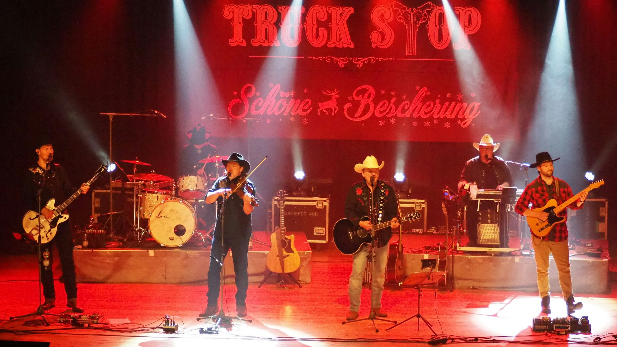 Sechs Musiker stehen auf einer rot beleuchteten Bühne.