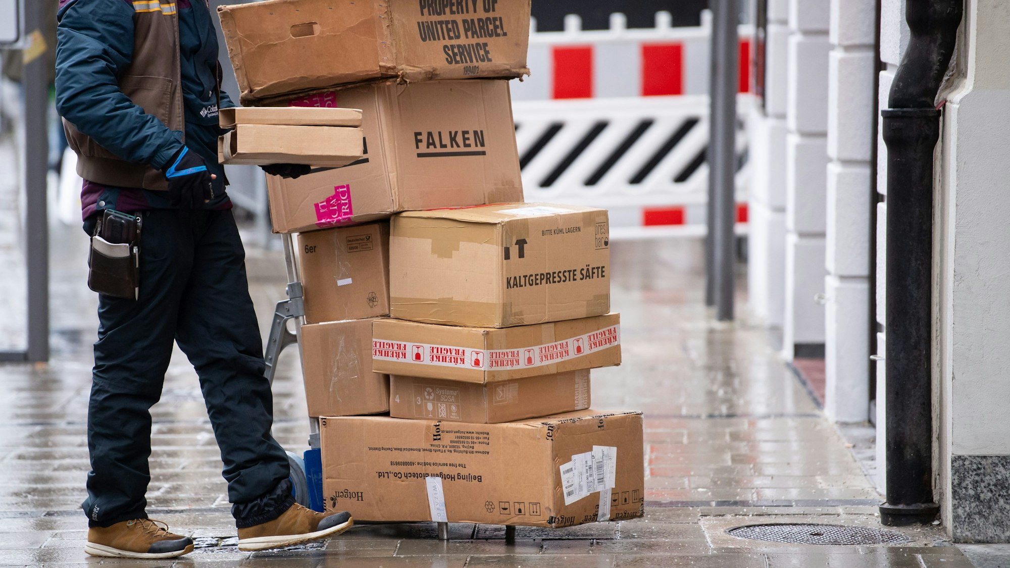 Ein Zusteller steht neben einer Sackkarre, auf der sich Pakete stapeln.