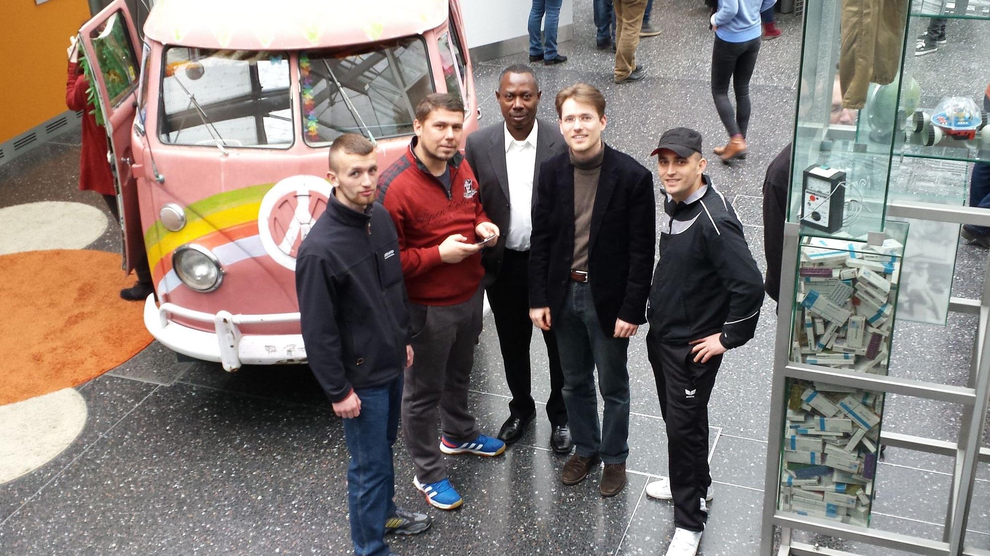 Mehrere junge Männer stehen vor einem bunt bemalten alten VW-Bus.