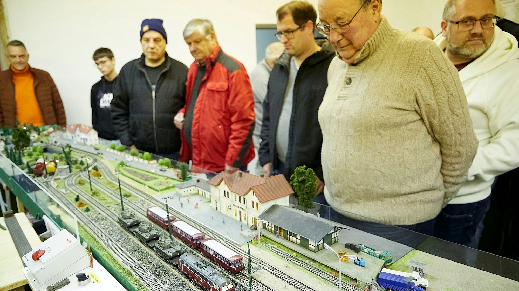 Um das Modell stehen mehrere Besucher. Sie blicken sehr interessiert auf die Züge, die Schienen und den Bahnhof im Kleinformat.