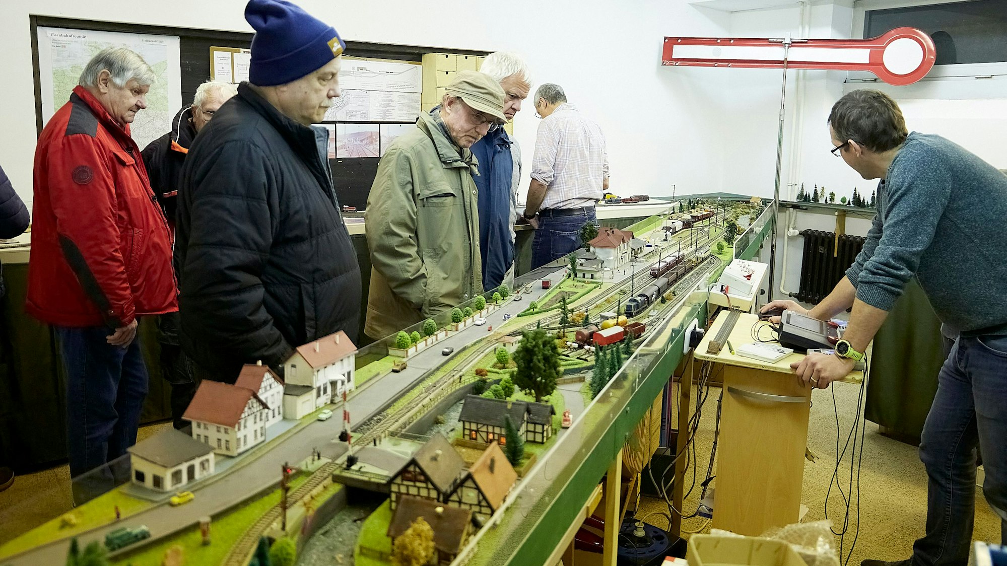 Mehrere Besucher stehen an dem Modell, das aus Häusern, Schienen und Grünlandschaft besteht.