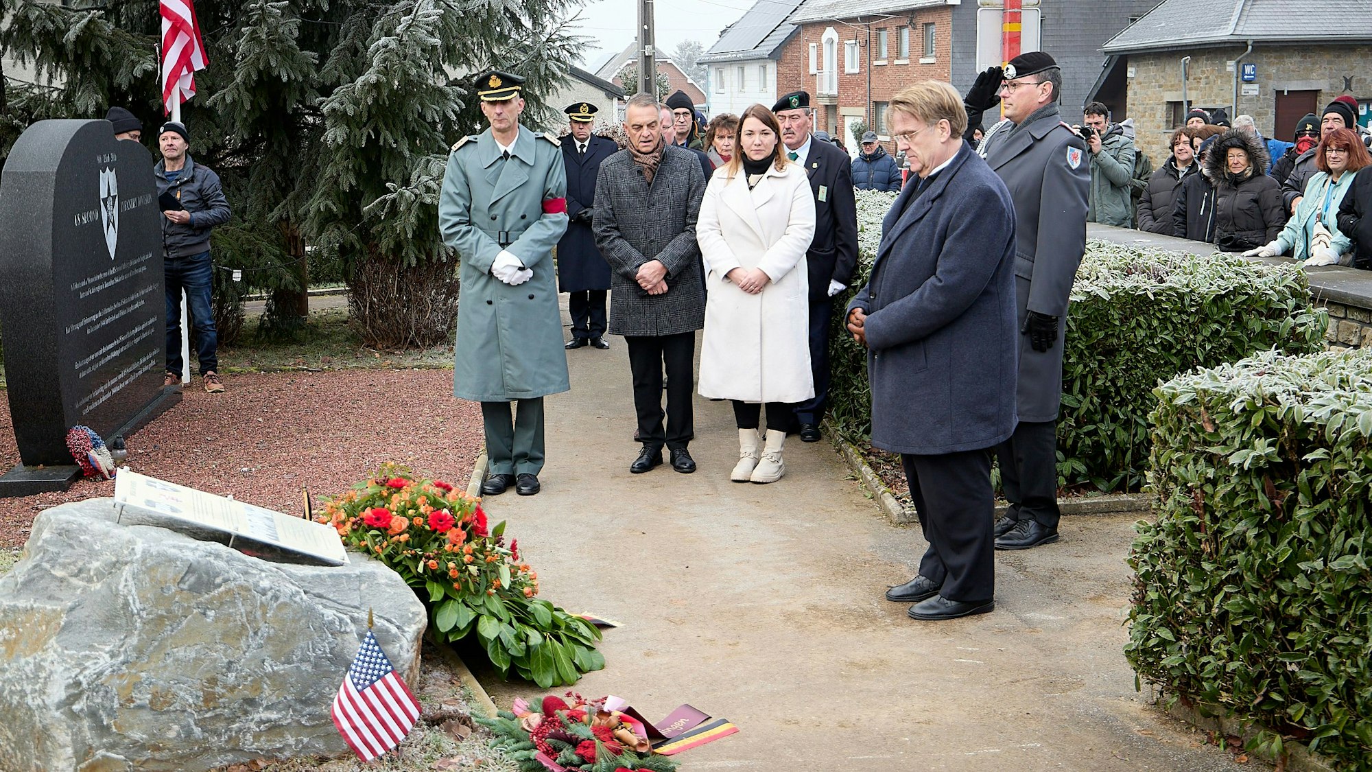 Die geladenen Gäste stehen schweigend vor einem großen Stein, an dem Kränze niedergelegt wurden. Daneben ist eine kleine US-amerikanische Flagge zu sehen.