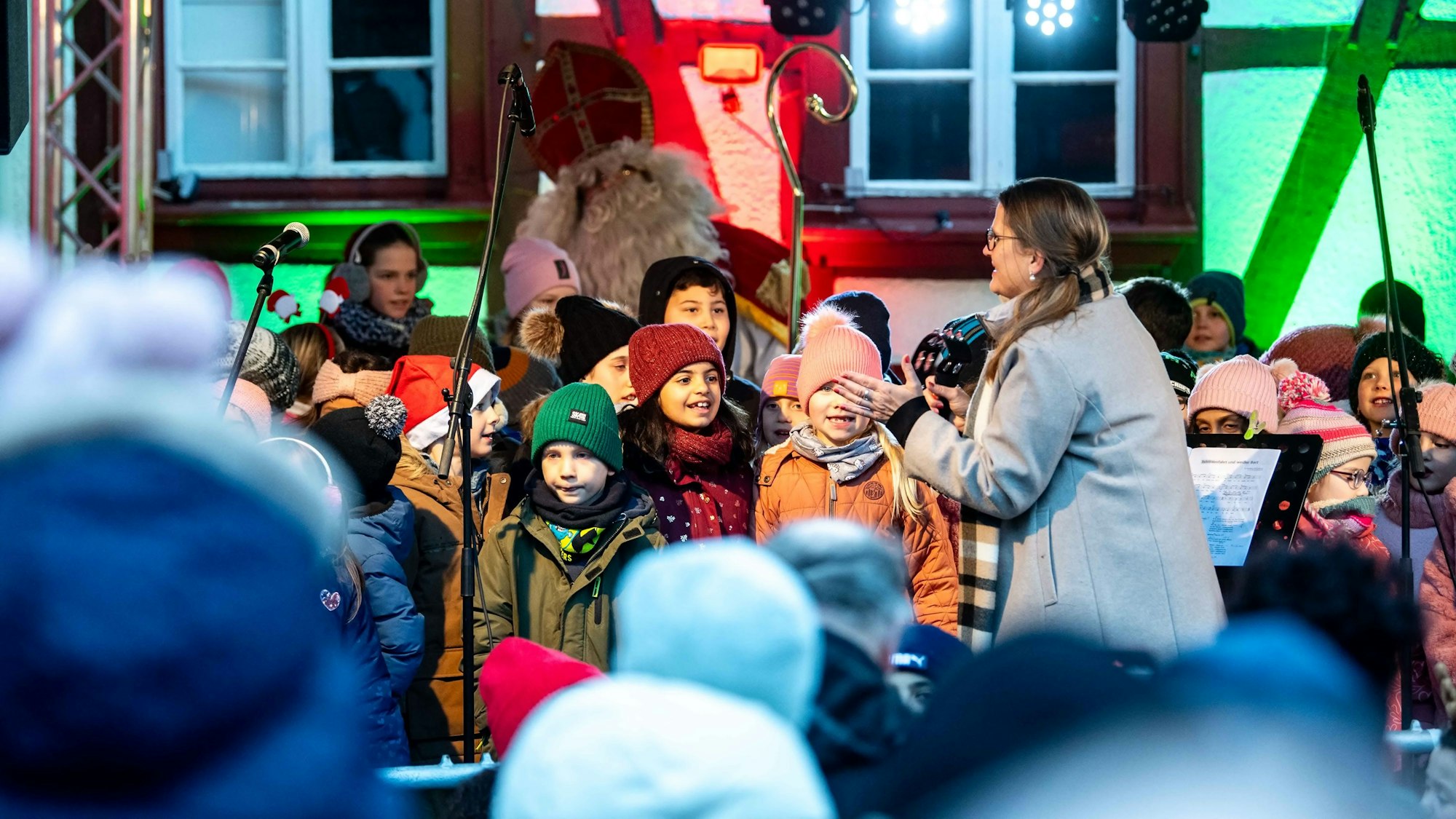 Das Bild zeigt einige Grundschüler, die auf einer Bühne stehen. Im Hintergrund ist der Nikolaus zu erkennen.