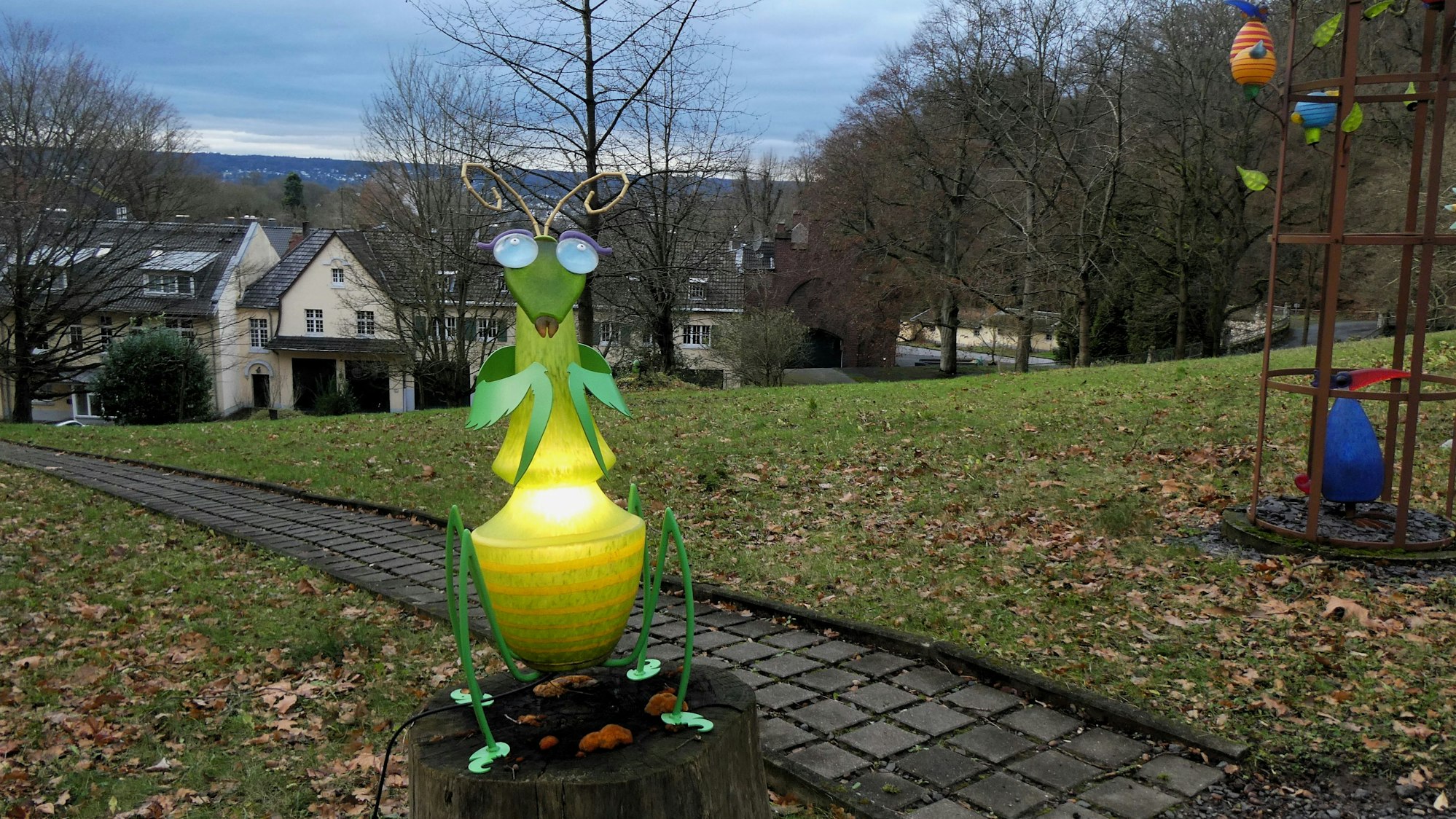 Eine grün-gelbe Plastik, die einen Grashüpfer darstellt, steht in einem großen Park.