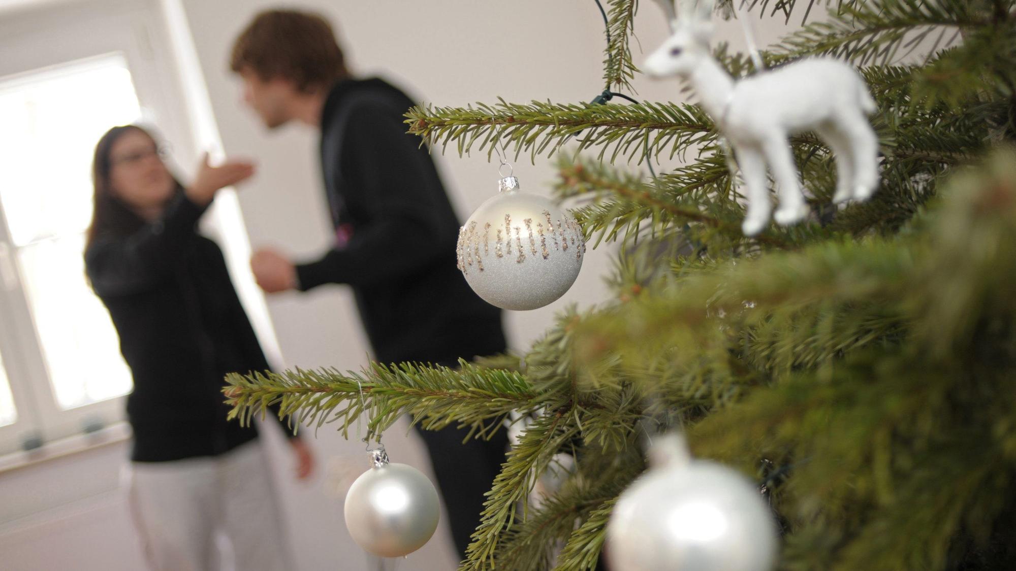 Hinter einem Weihnachtsbaum streiten sich zwei Personen.