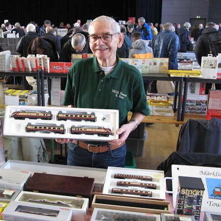 Ein 83 Jahre alter Mann hält eine offene Packung mit Modellbahnwagen in den Händen.
