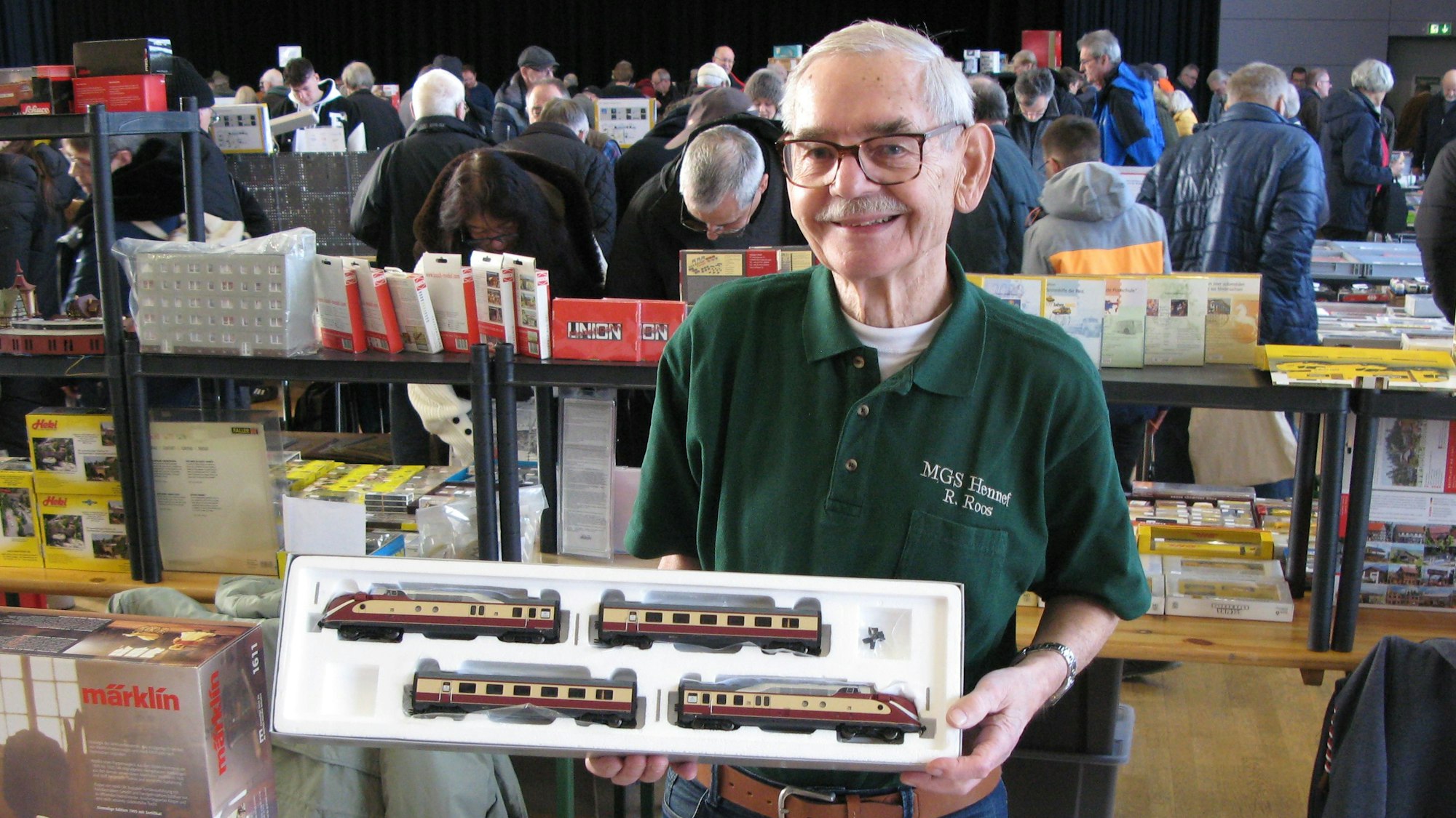 Ein 83 Jahre alter Mann hält eine offene Packung mit Modellbahnwagen in den Händen.