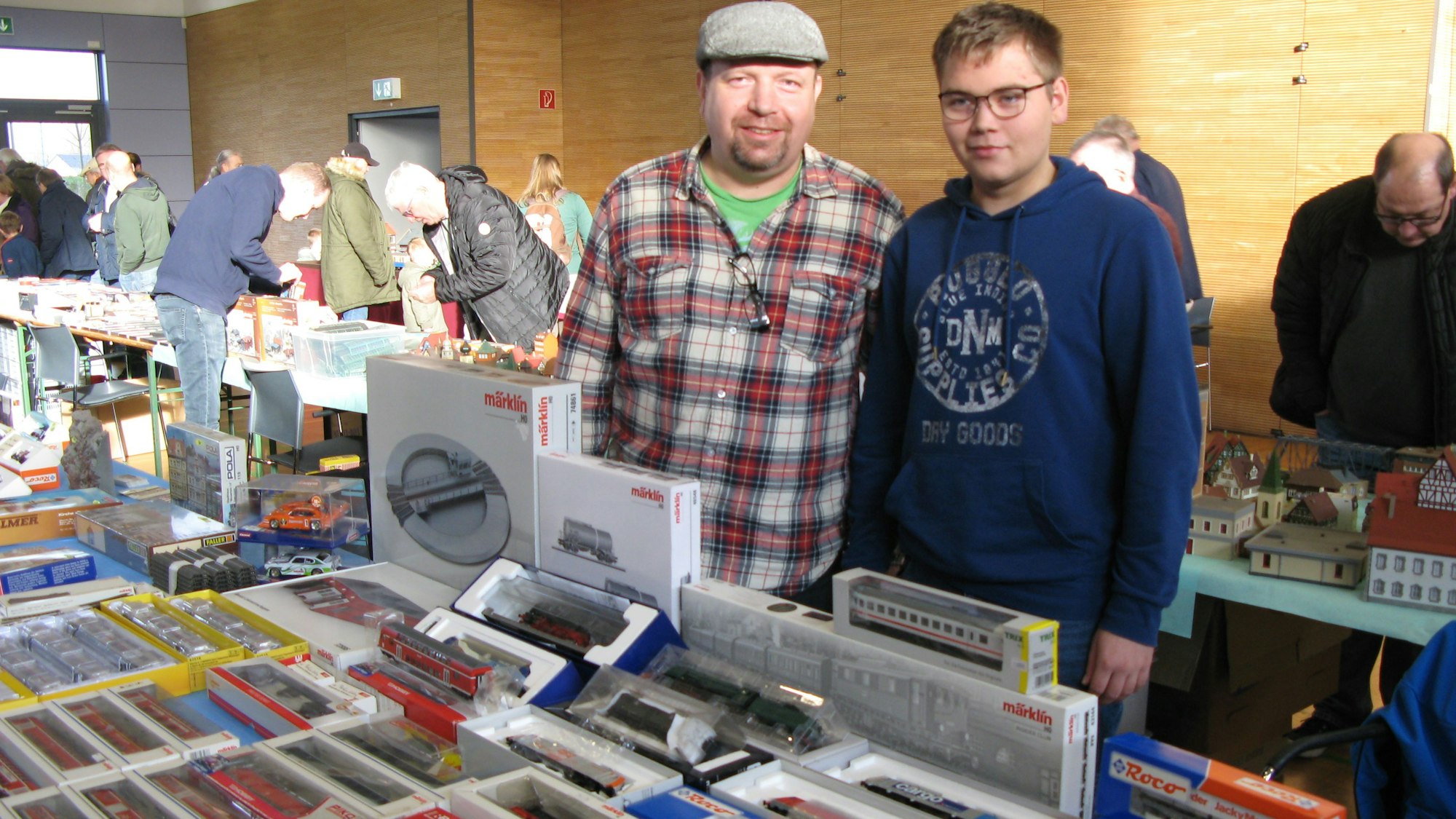 Vater und Sohn stehen hinter einem Verkaufstisch mit Modelleisenbahn-Lokomotiven und Wagen.