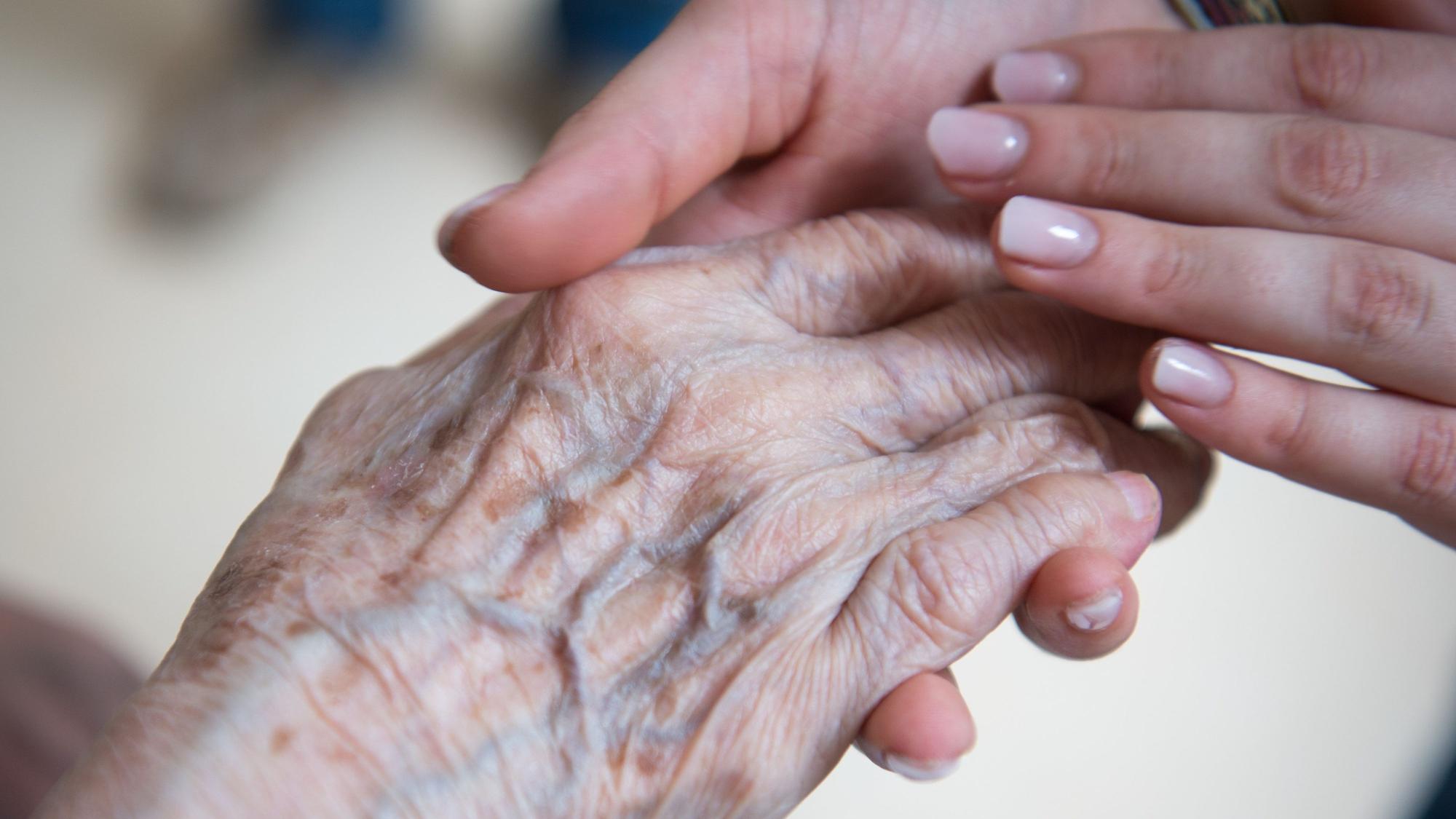 Eine jung Frau hält die Hand einer alten Frau.