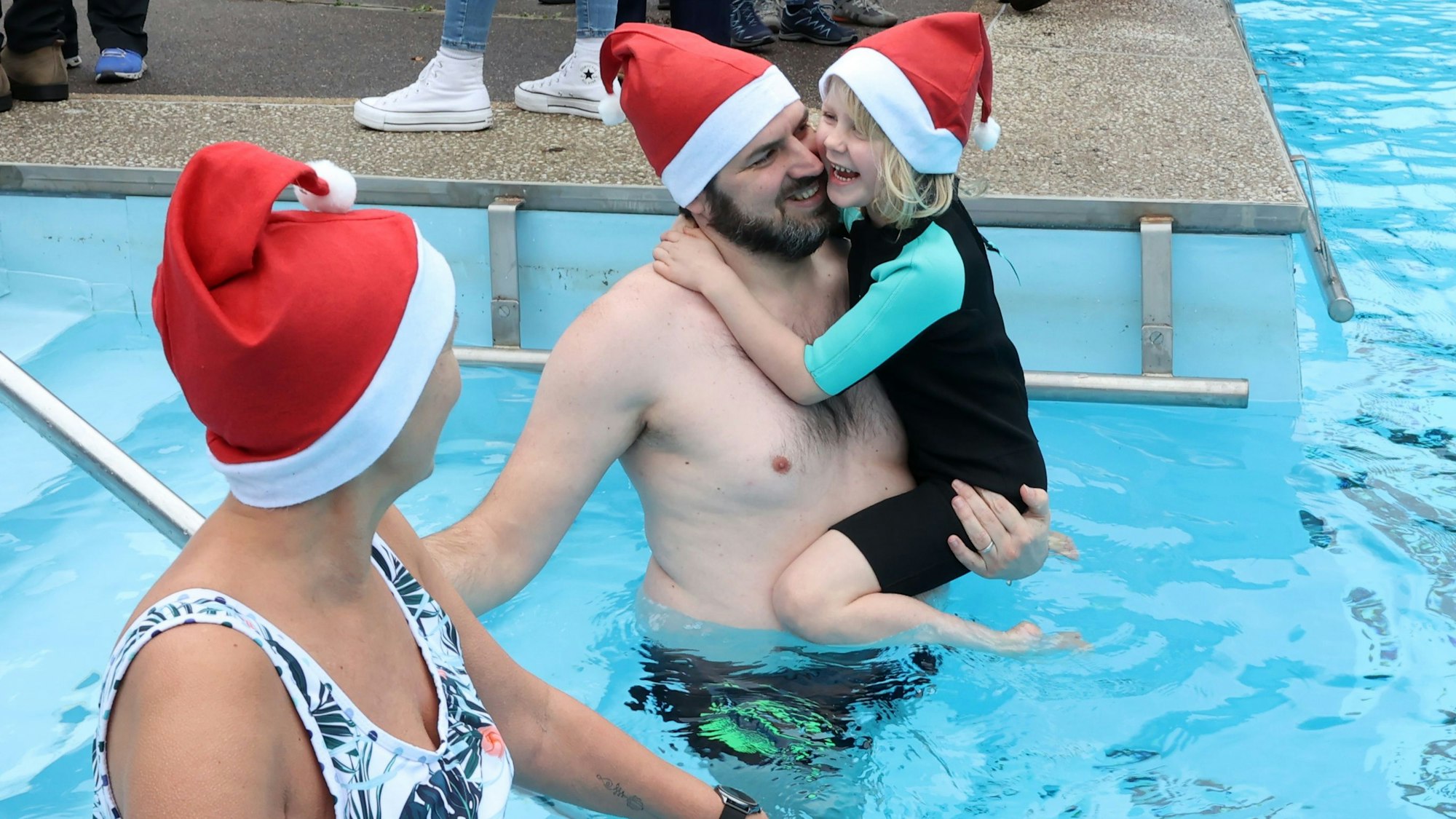 Ein Mann trägt seine kleine Tochter in ein Außen-Schwimmbecken im Winter.