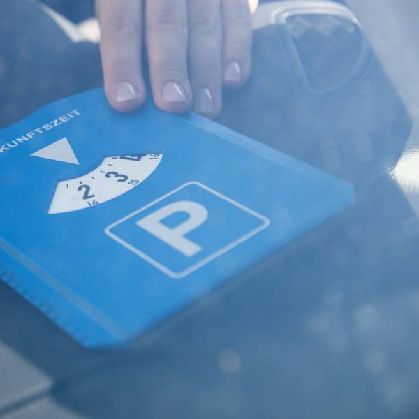 Eine Frau legt eine Parkscheibe vor die Scheibe vorne ins Auto.