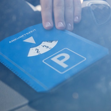 Eine Frau legt eine Parkscheibe vor die Scheibe vorne ins Auto.