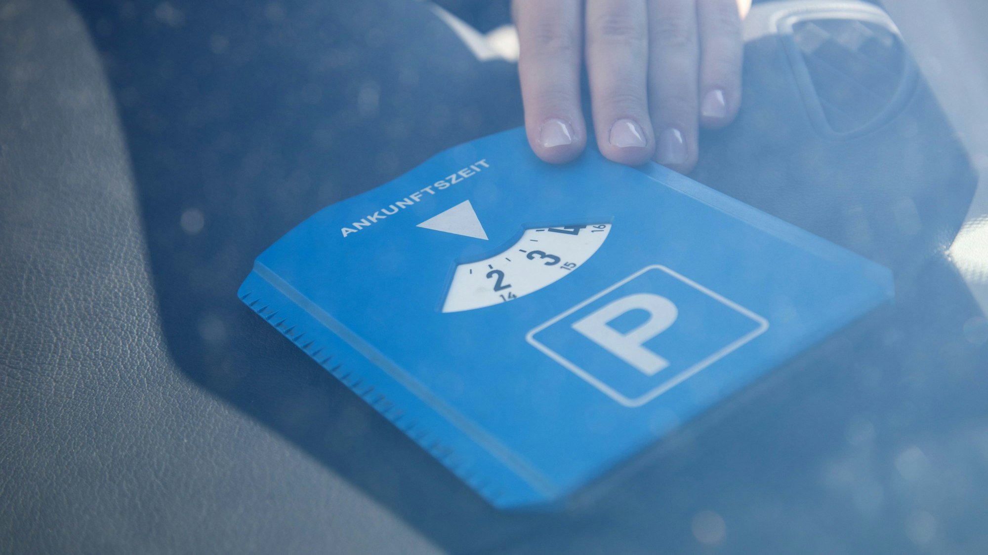 Eine Frau legt eine Parkscheibe vor die Scheibe vorne ins Auto.