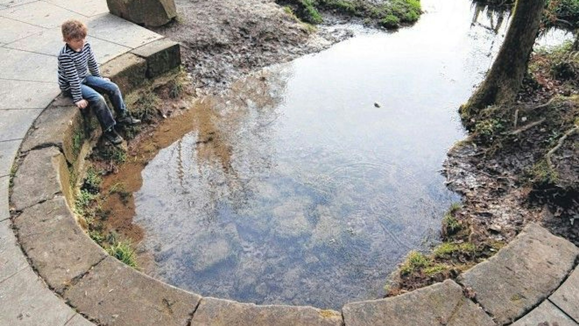 Ein Kind sitzt an der Quelle der Strunde.