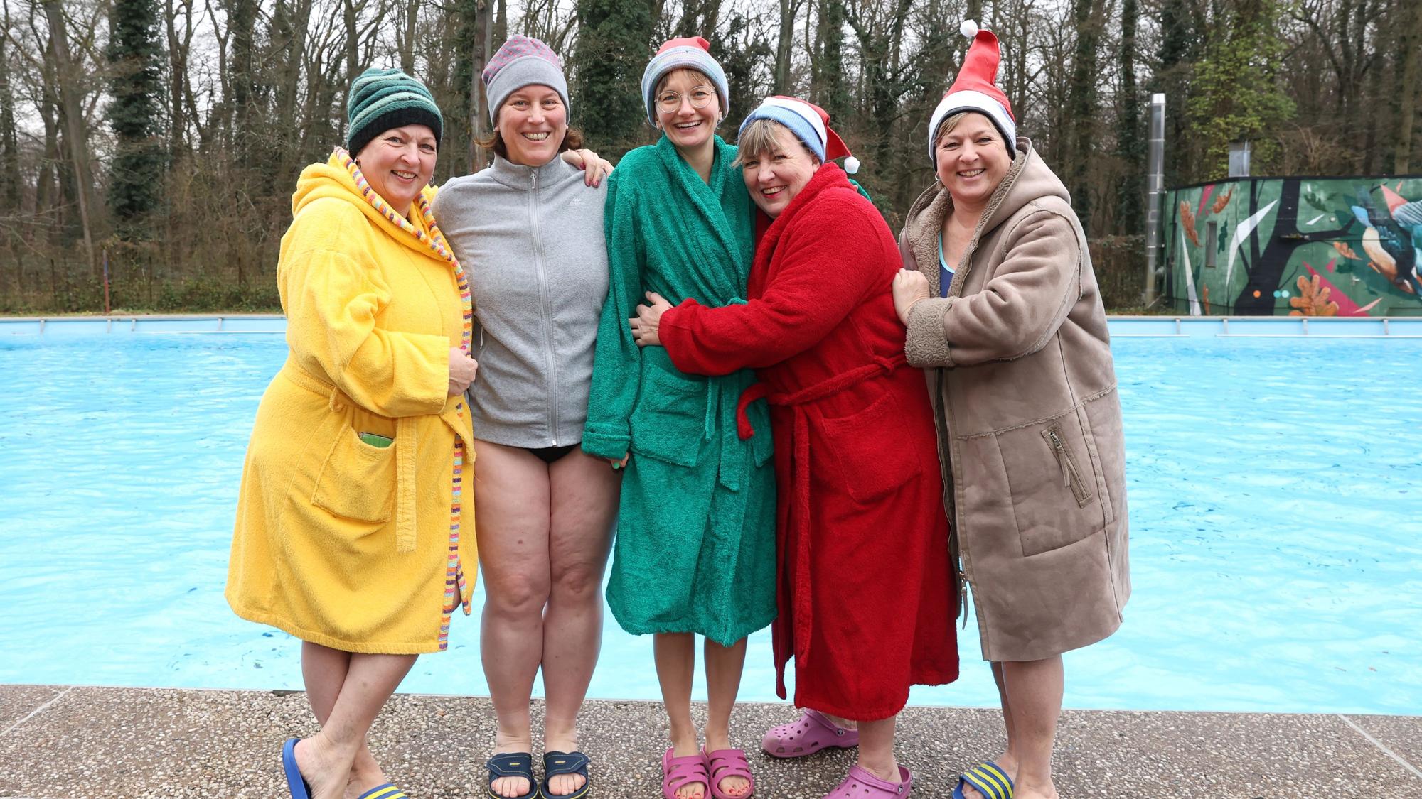Fünf Frauen in bunten Bademänteln stehen draußen am Beckenrand eines Schwimmbeckens.