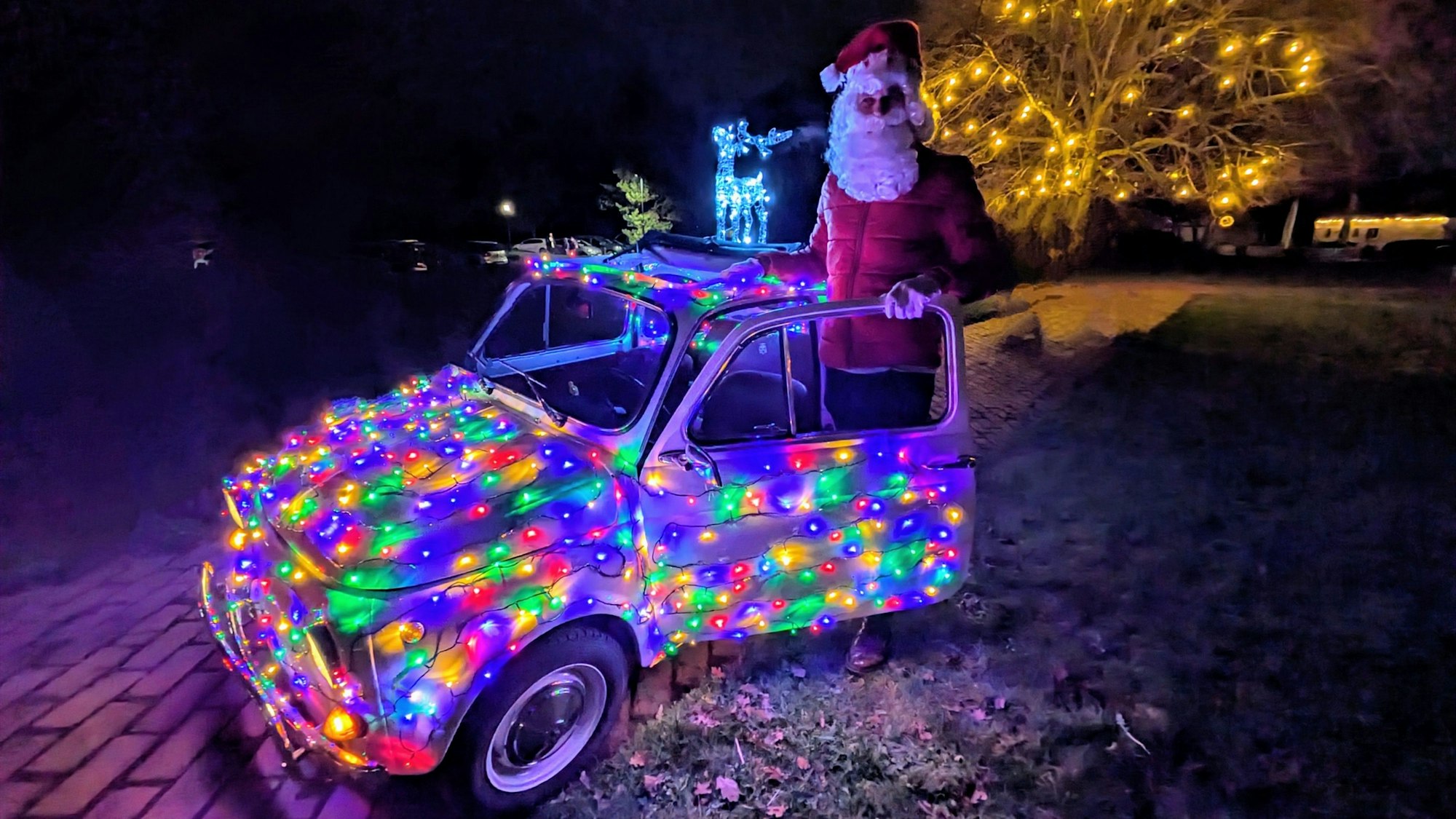 "Weihnachtsmann" Guido Schäfer steht vor seinem bunt beleuchteten Fiat 500.