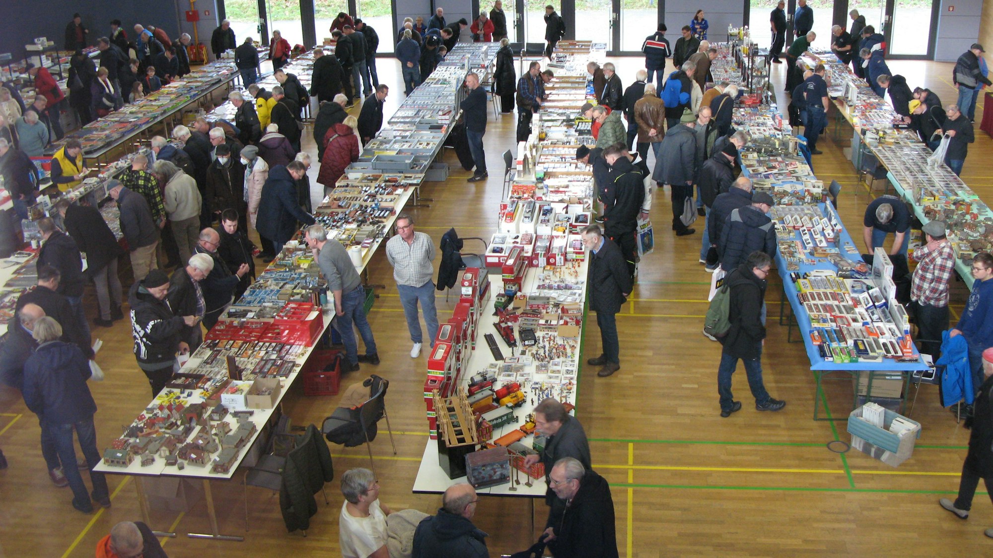 Blick von oben in eine Halle mit langen Tischreihen, auf denen Modellbahnartikel aller liegen, und zahlreichen Menschen.