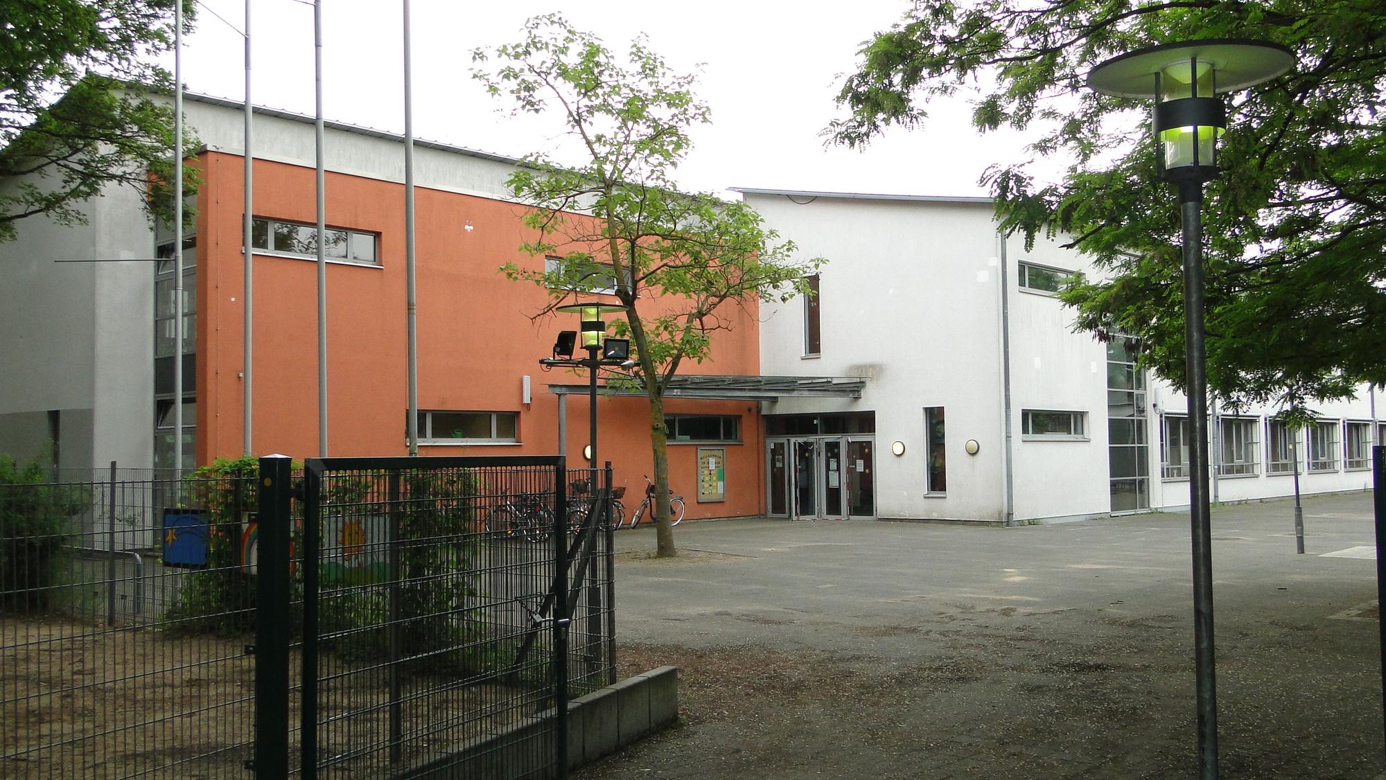 Blick auf eine Schule mit Schulhof und Bäumen davor