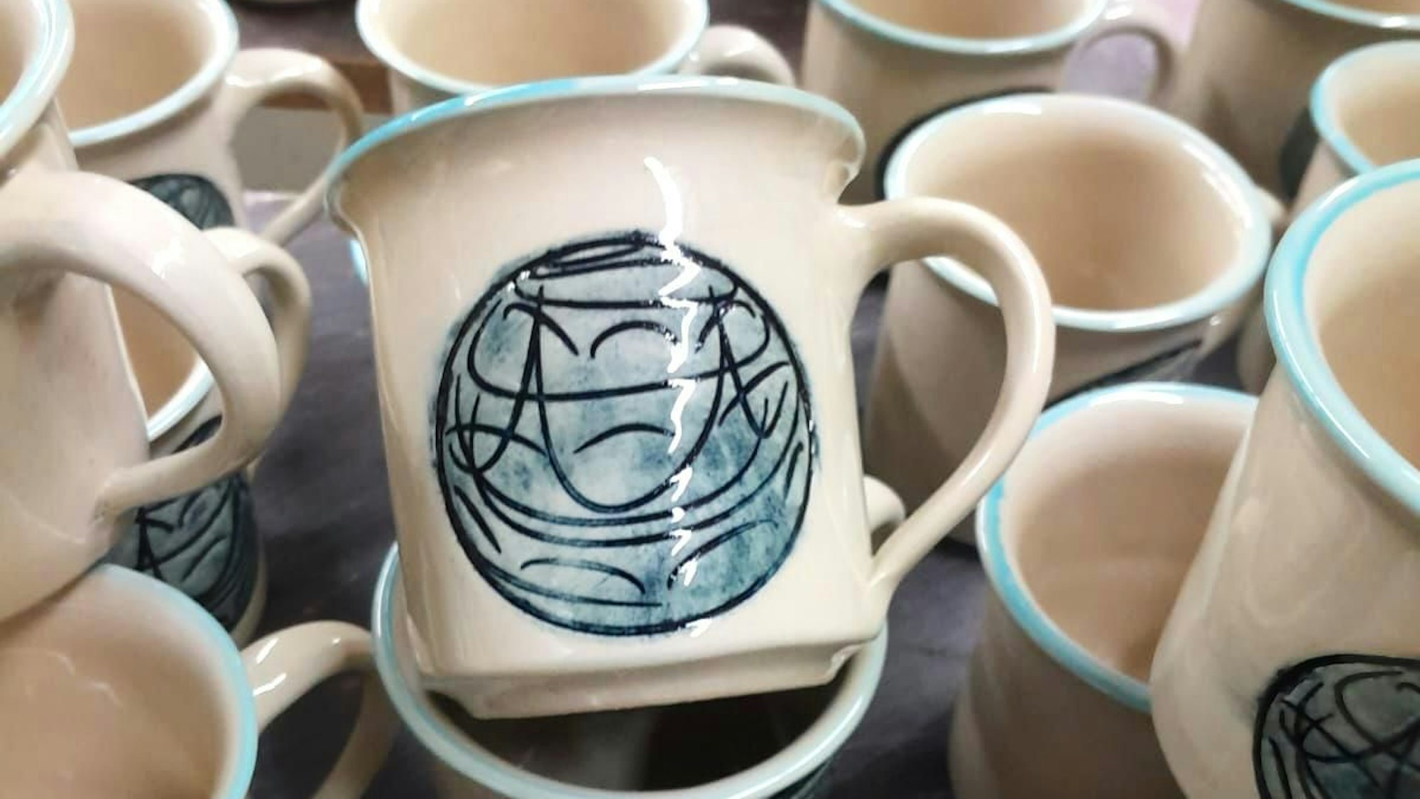 Eine weiße Tasse mit einem hellblauen Kreis, den ein Muster aus geschwungenen schwarzen Linien füllt.