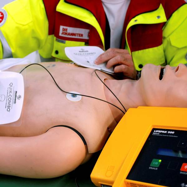 Ein Rettungssanitäter präsentiert einen öffentlich zugänglichen Defibrillator an einer Puppe.