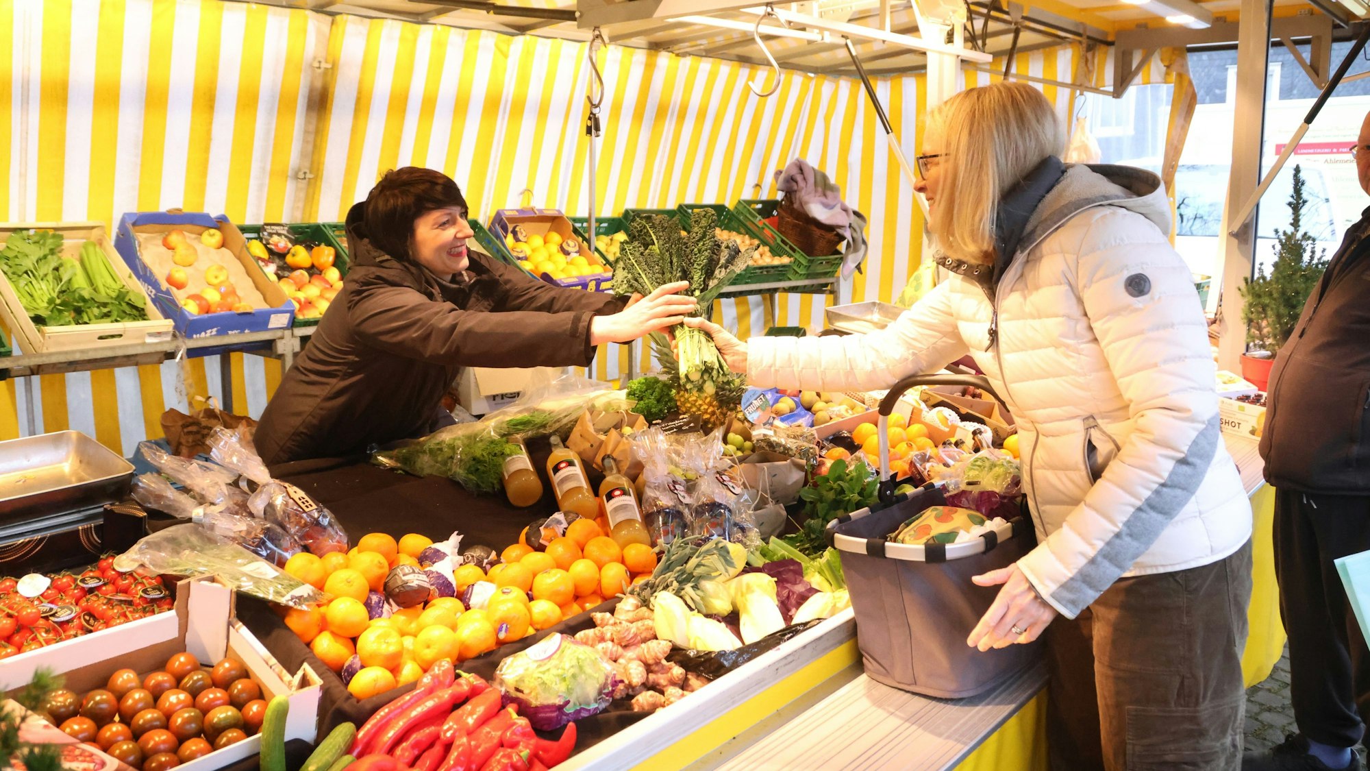 Eine Frau verkauft an ihrem Gemüsestand auf dem Wochenmarkt in Gummersbach Hülsenbusch Ware an eine Kundin.