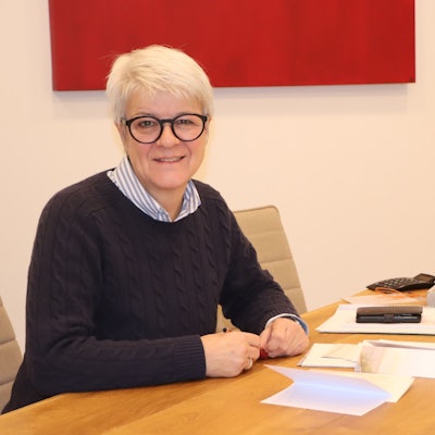 Auf dem Bild ist die Bestatterin zu sehen, die an einem großen Tisch sitzt.