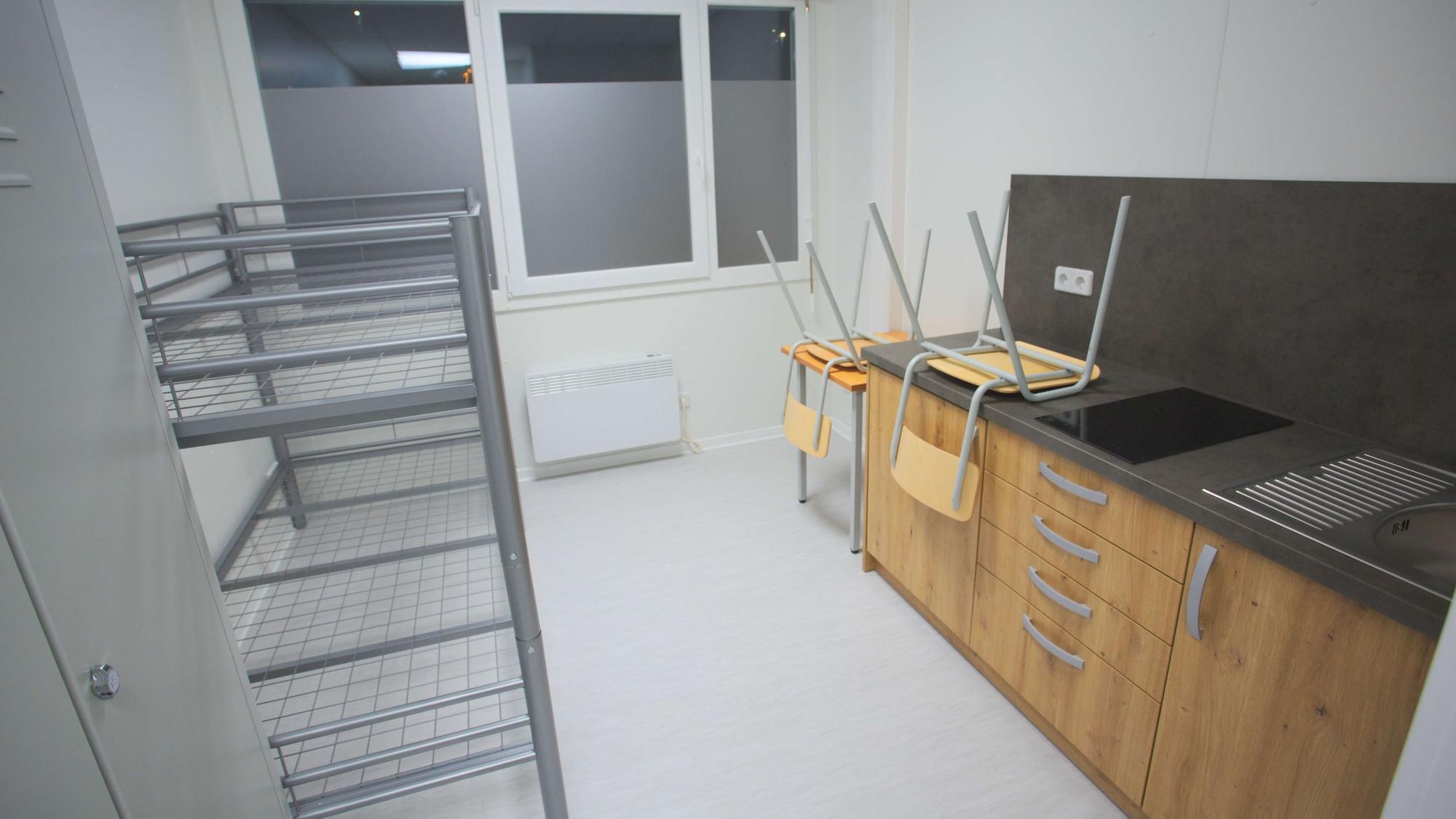 Innenansicht eines Containers für Geflüchtete – mit Küchenzeile, Hochbett, einem Tisch und zwei Stühlen.