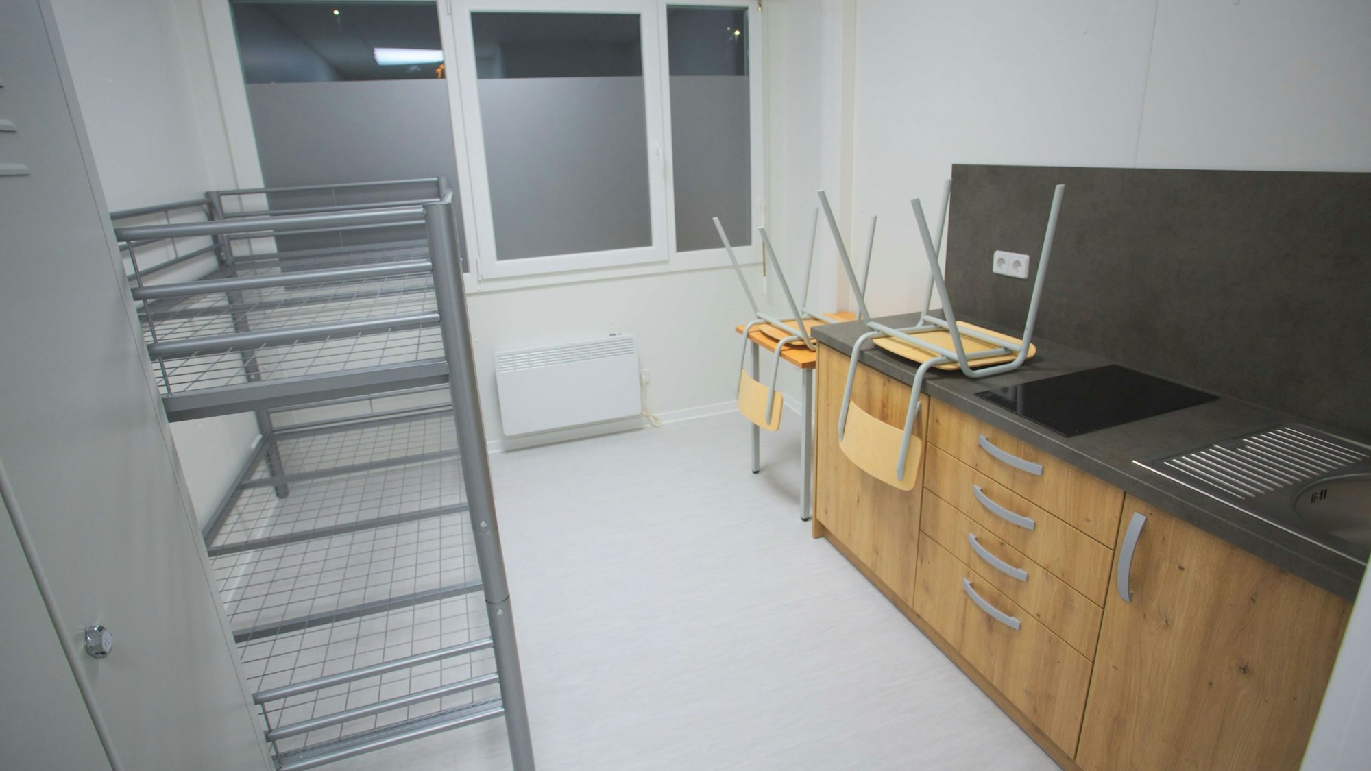 Innenansicht eines Containers für Geflüchtete – mit Küchenzeile, Hochbett, einem Tisch und zwei Stühlen.