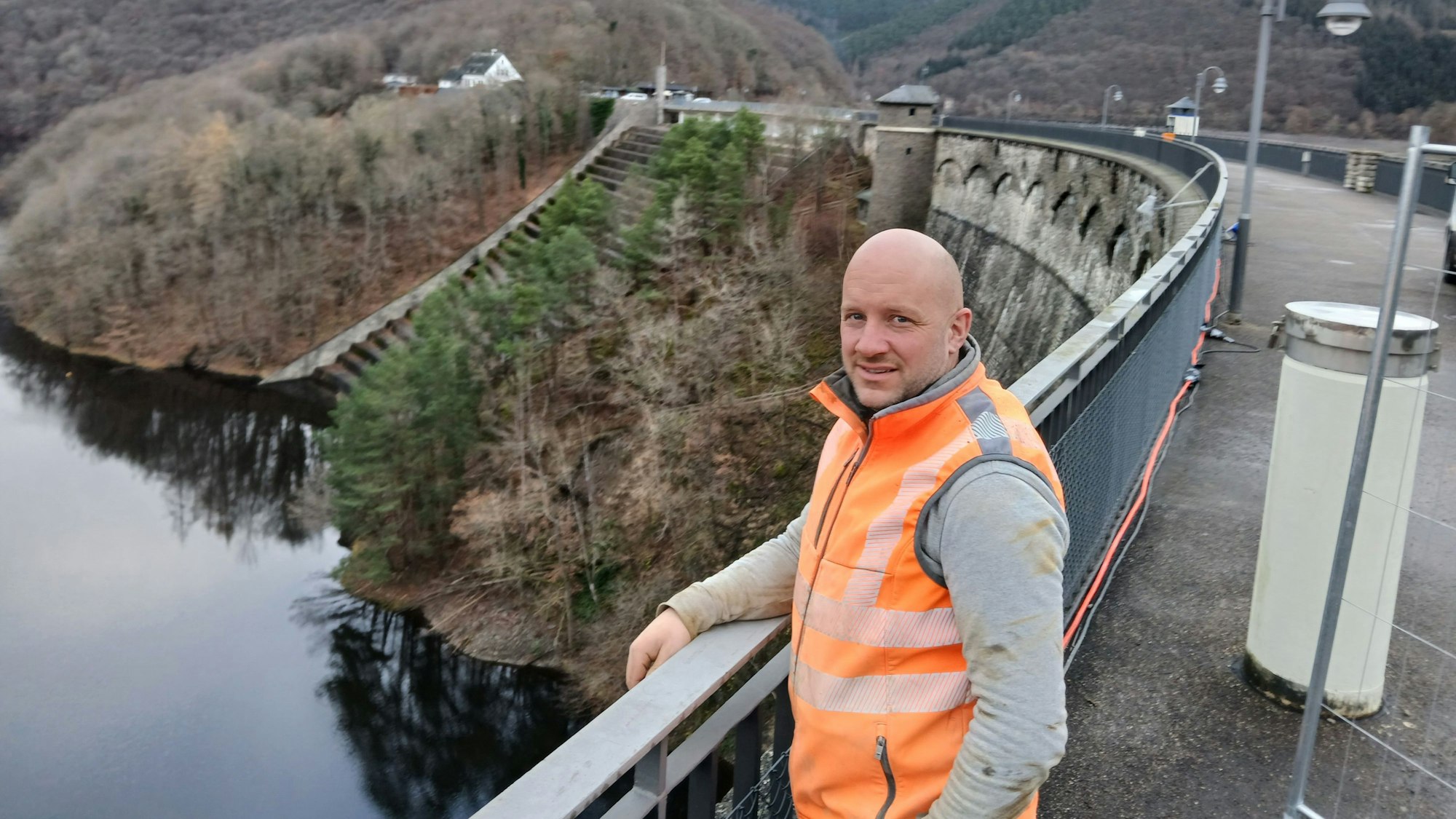 Gerrit Jaspers trägt eine orangefarbene Warnweste und steht auf der Dammkrone der Urftstaumauer.
