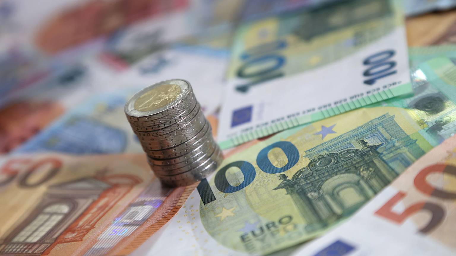Ein Stapel mit Zwei-Euro-Münzen steht auf verschiedenen Euro-Banknoten.