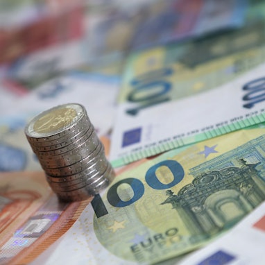 Ein Stapel mit Zwei-Euro-Münzen steht auf verschiedenen Euro-Banknoten.