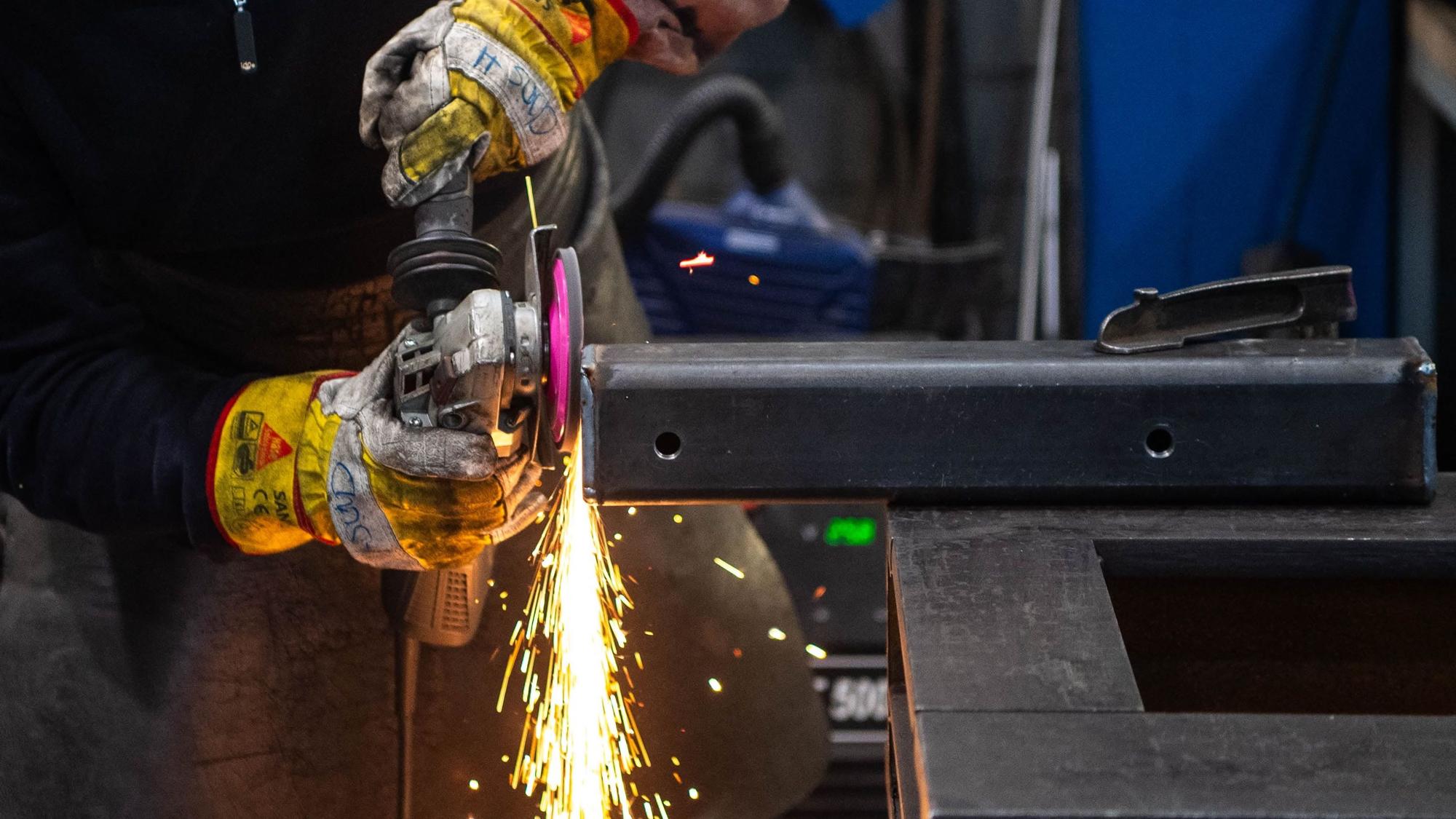 Das Bild zeigt einen Metallbauer, der eine Metallkonstruktion abschleift.