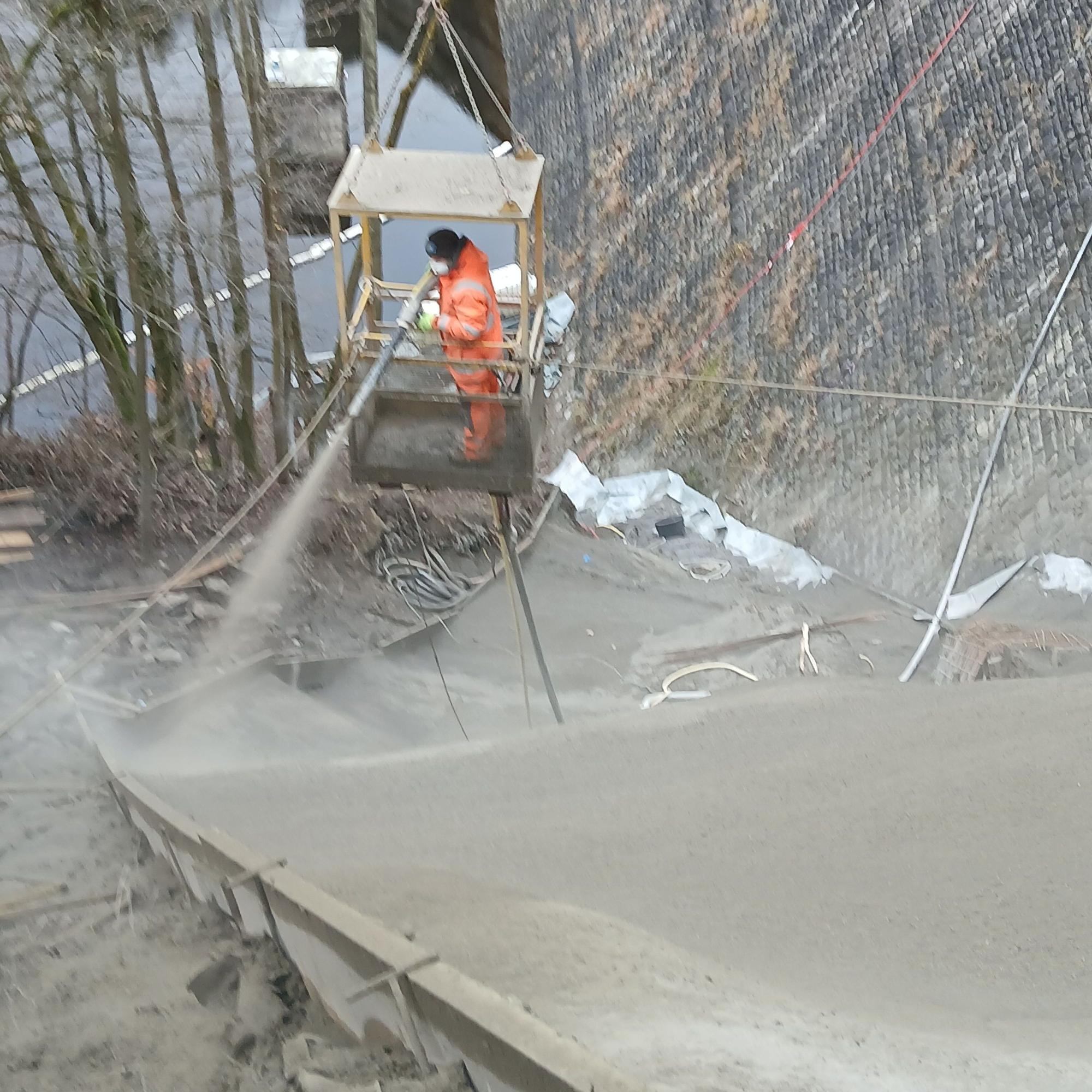 Mit einer Spritzdüse wird der Beton von einem Arbeiter in den Hang neben der Staumauer eingebracht.