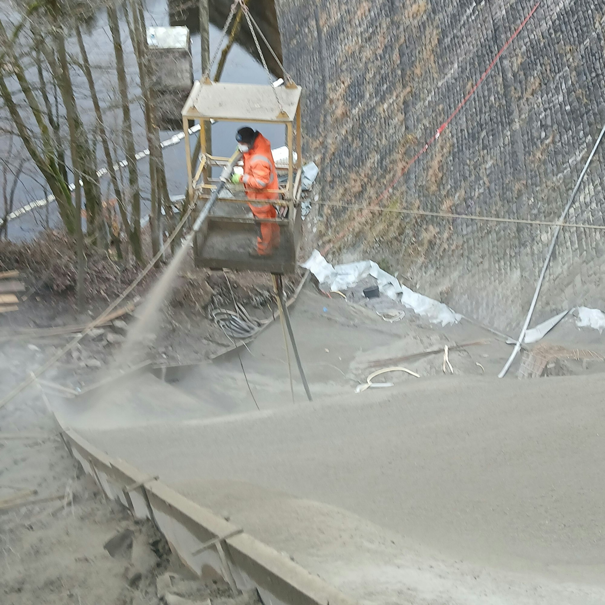 Mit einer Spritzdüse wird der Beton von einem Arbeiter in den Hang neben der Staumauer eingebracht.