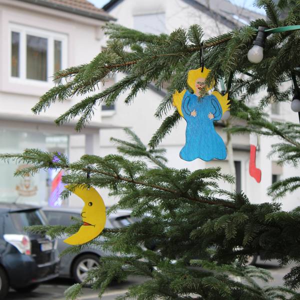 Ein Engel und ein Halbmond hängen an einem geschmückten Tannenbaum im Freien.