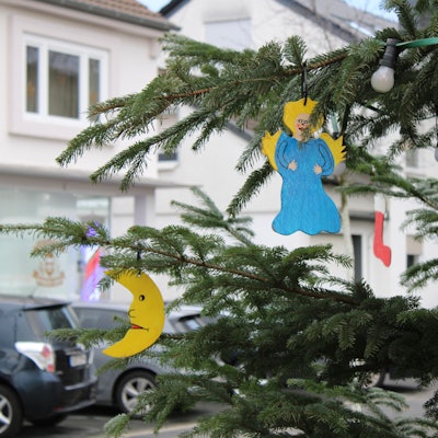 Ein Engel und ein Halbmond hängen an einem geschmückten Tannenbaum im Freien.