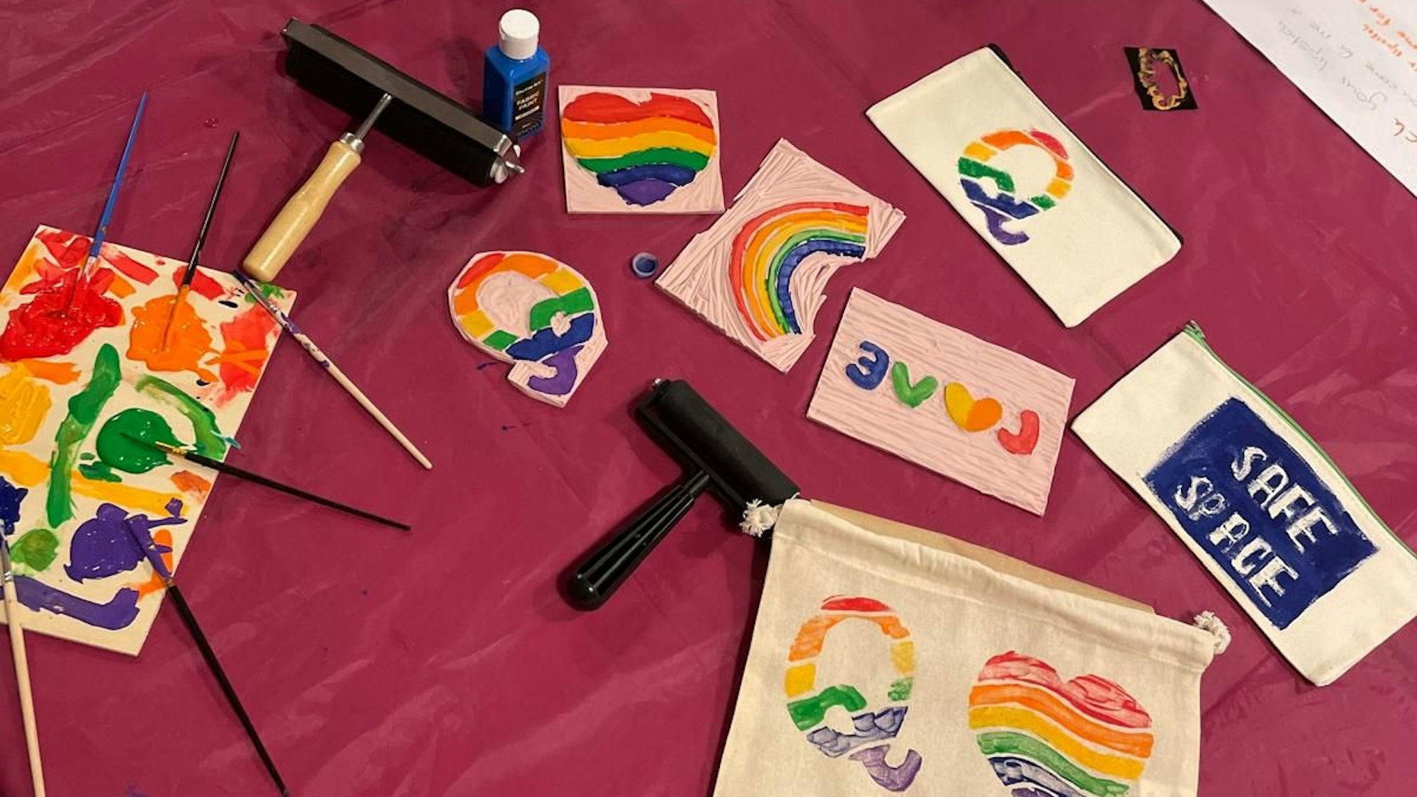 Mit Linoldruck bunt gefärbte Beutel und Mäppchen zeigen Herzen in Regenbogenfarben, die Aufschrift "Q" und "Safe Space".