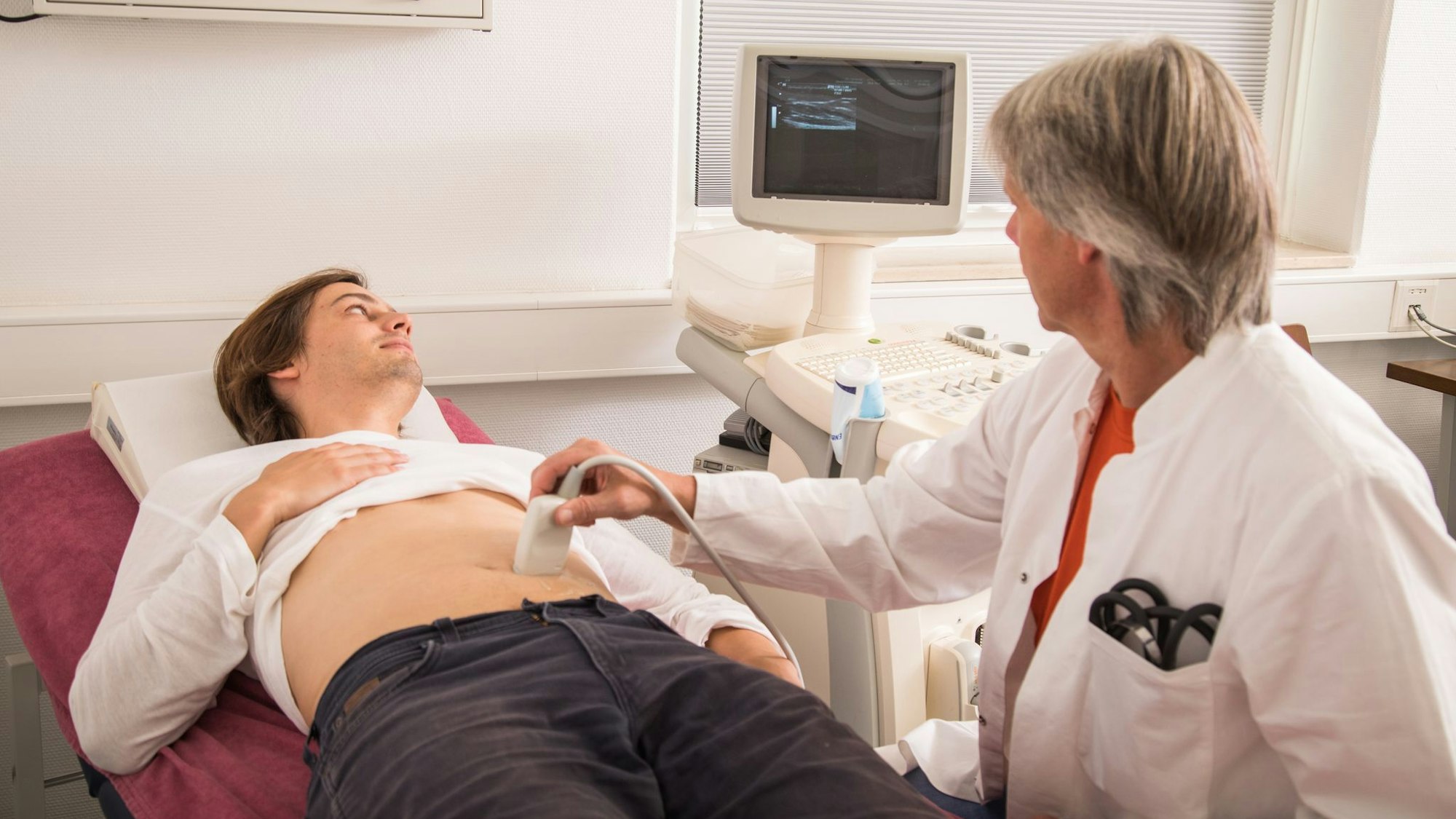 Bei einem Mann, der auf einer Liege liegt, wird ein Ultraschall am Bauch durchgeführt.
