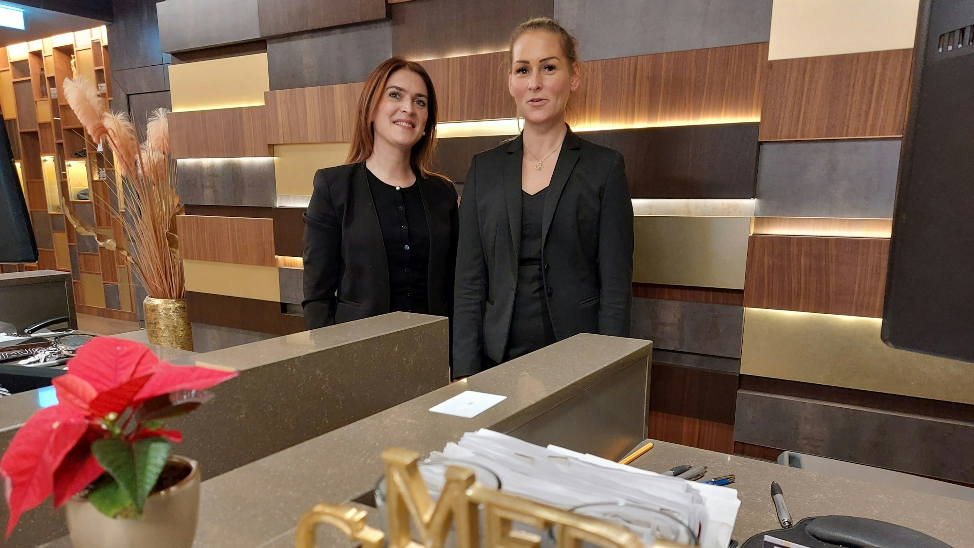 Zwei Frauen in schwarzem Oberteil und Sakko stehen an der Rezeption eines Hotels.