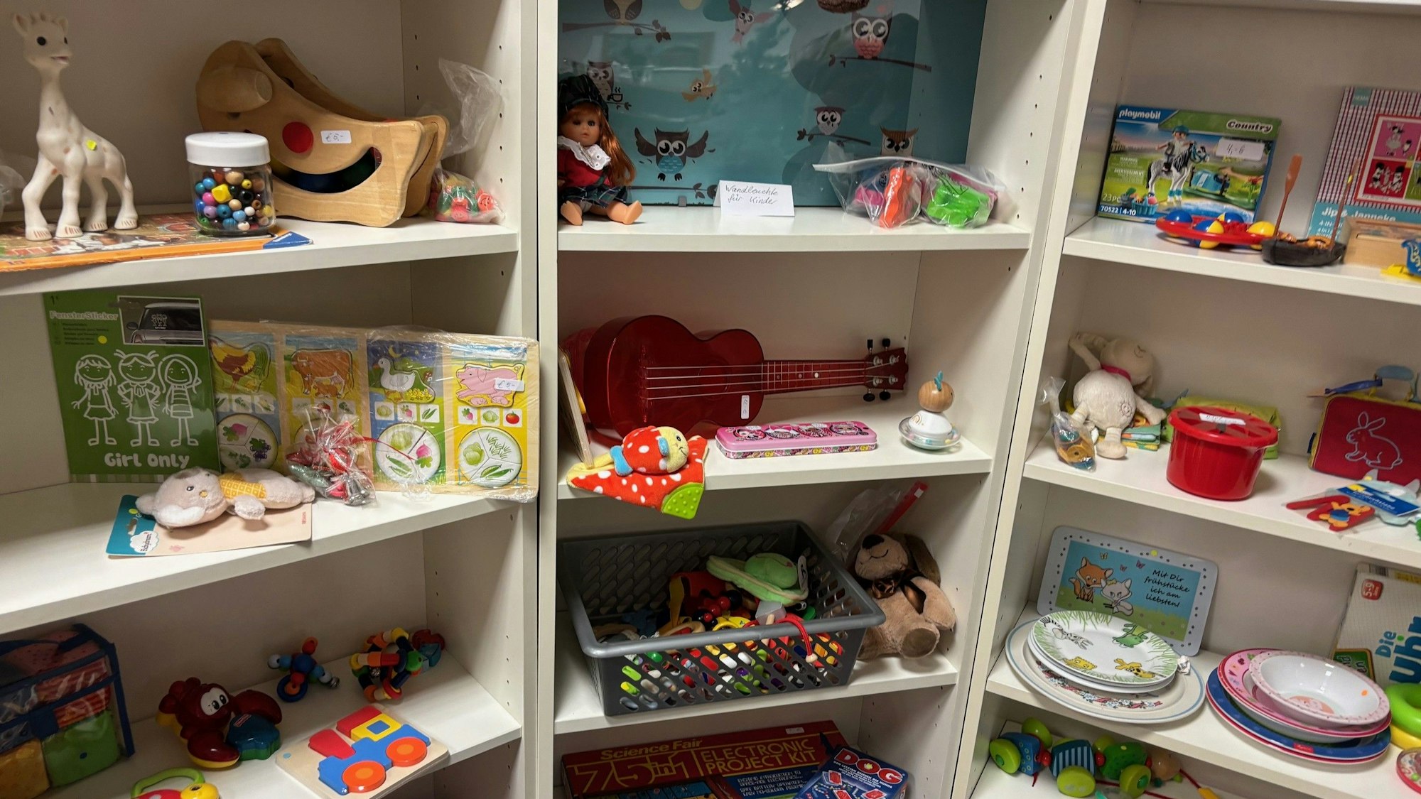 Auf dem Bild sind Spielsachen in einem weißen Holzregal zu sehen.