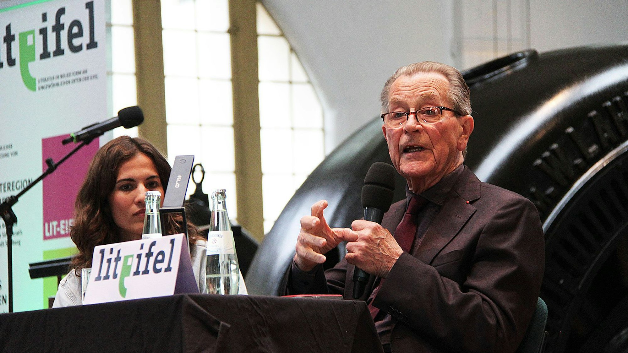 Franz Münterfering bei seiner Lesung im Jugendstilkraftwerk. Hinter ihm eine der mächtigen schwarzen Turbinen für die Energiegewinnung.