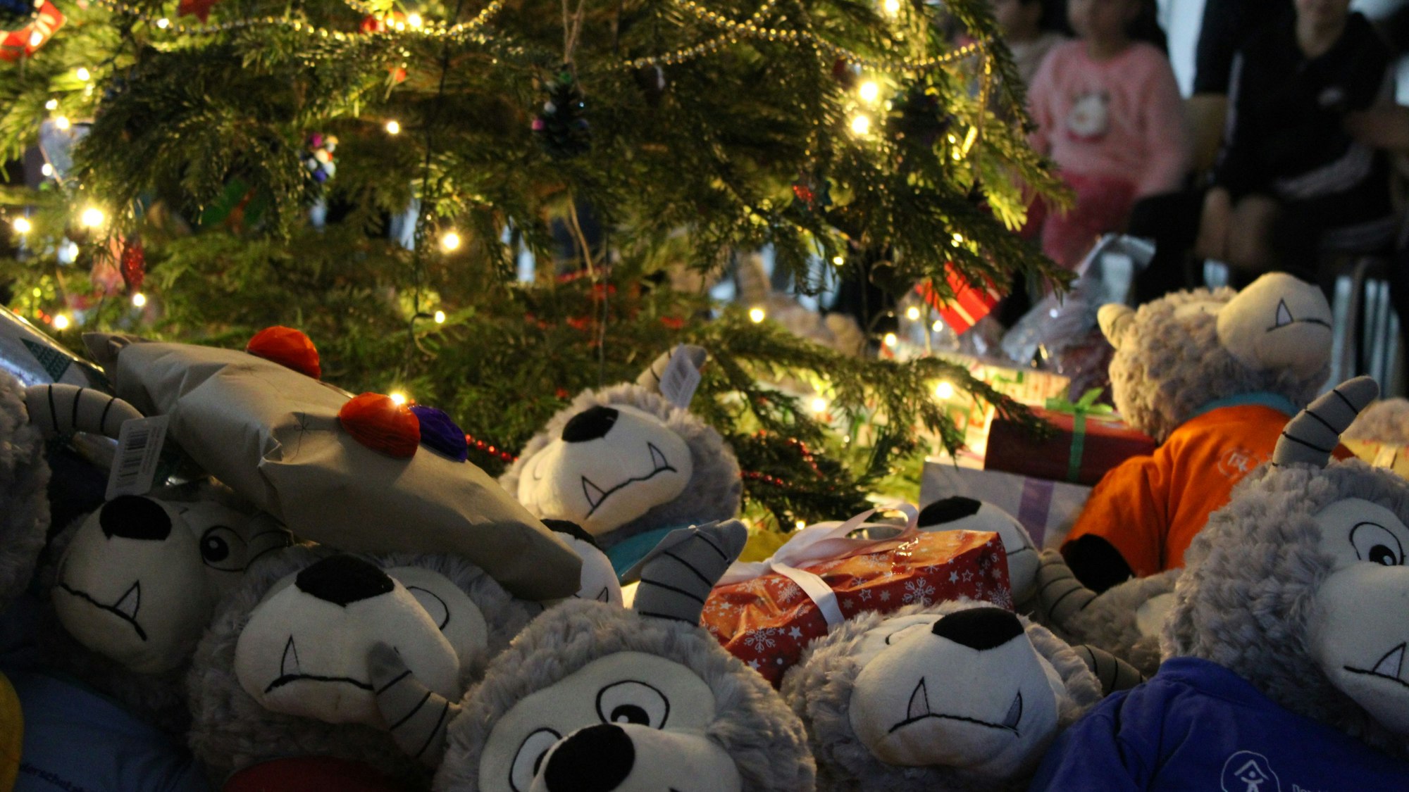 Plüschtiere und verpackte Geschenke liegen unter einem beleuchteten Weihnachtsbaum.