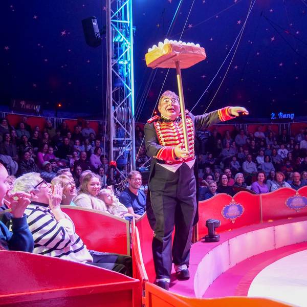 Das Foto zeigt den Clown mit einer Jonglage-Nummer vor den Rängen rund um die Manege.