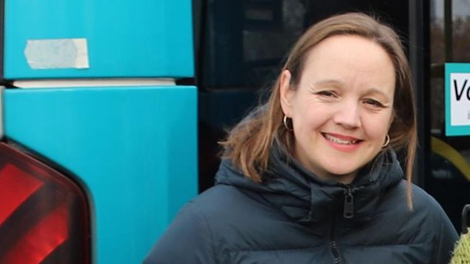 Eine Frau in einem blauen Daunenmantel steht vor einem Bus.