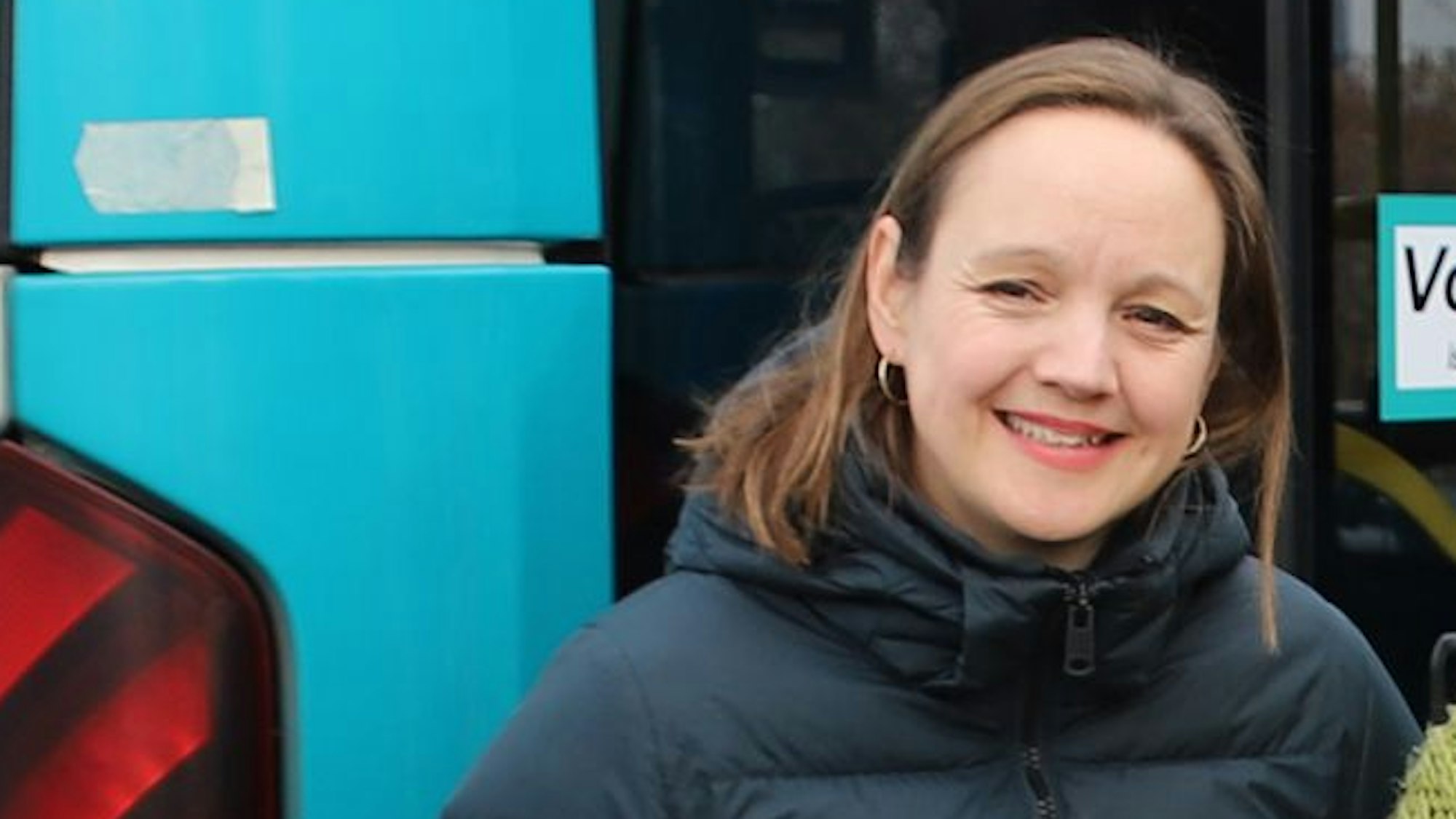 Eine Frau in einem blauen Daunenmantel steht vor einem Bus.