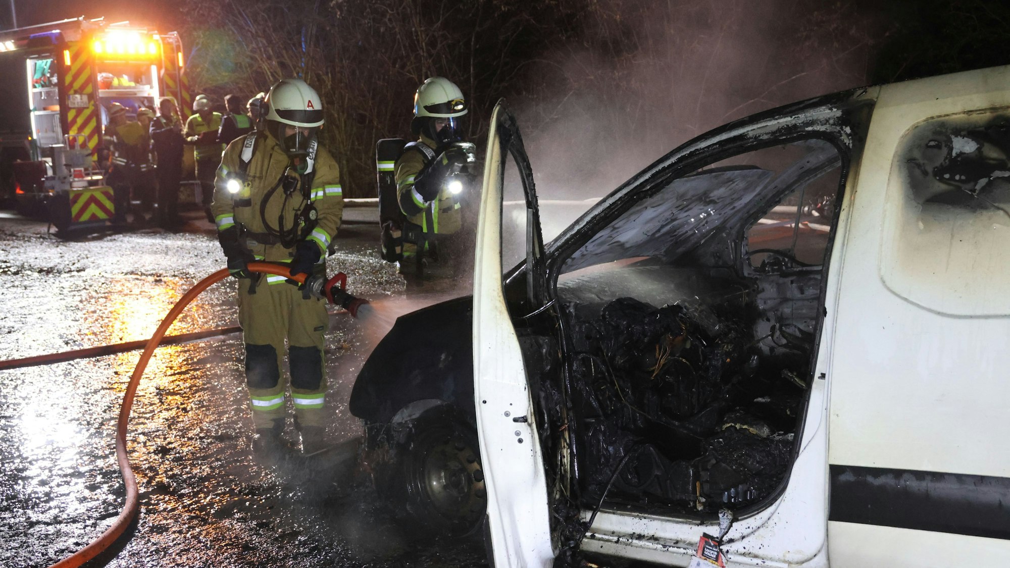 Feuerwehrleute löschen einen brennenden Pkw-Transporter.