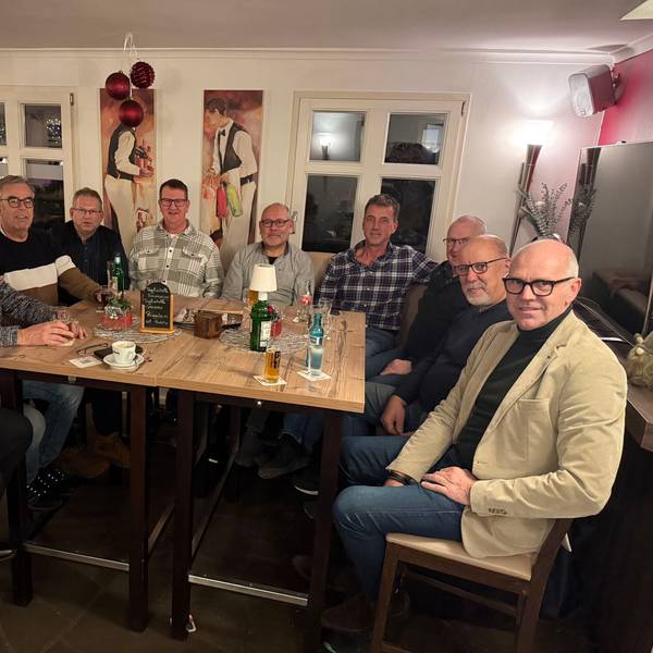 Eine Gruppe von zehn Männern sitzt um den Tisch einer Kneipe.