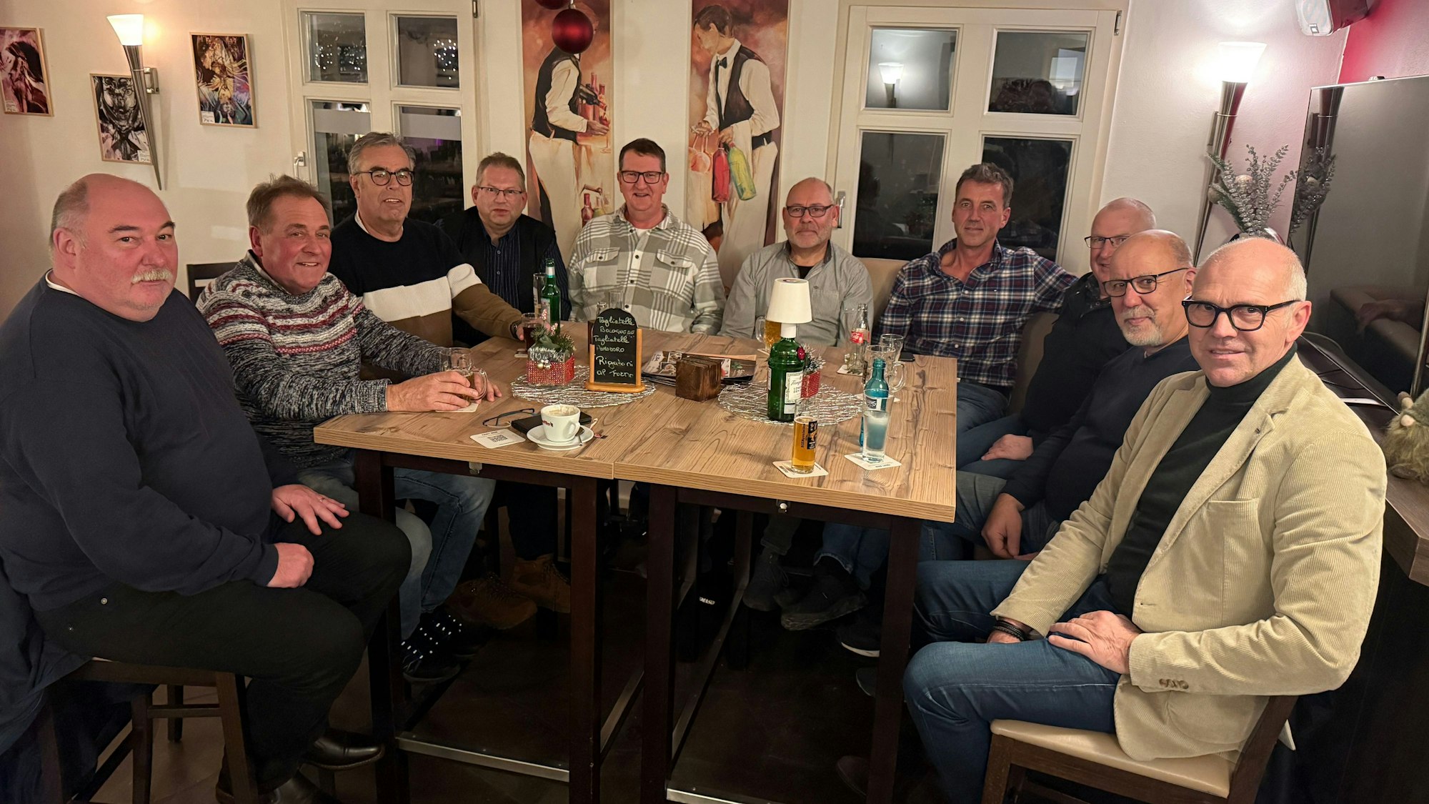 Eine Gruppe von zehn Männern sitzt um den Tisch einer Kneipe.